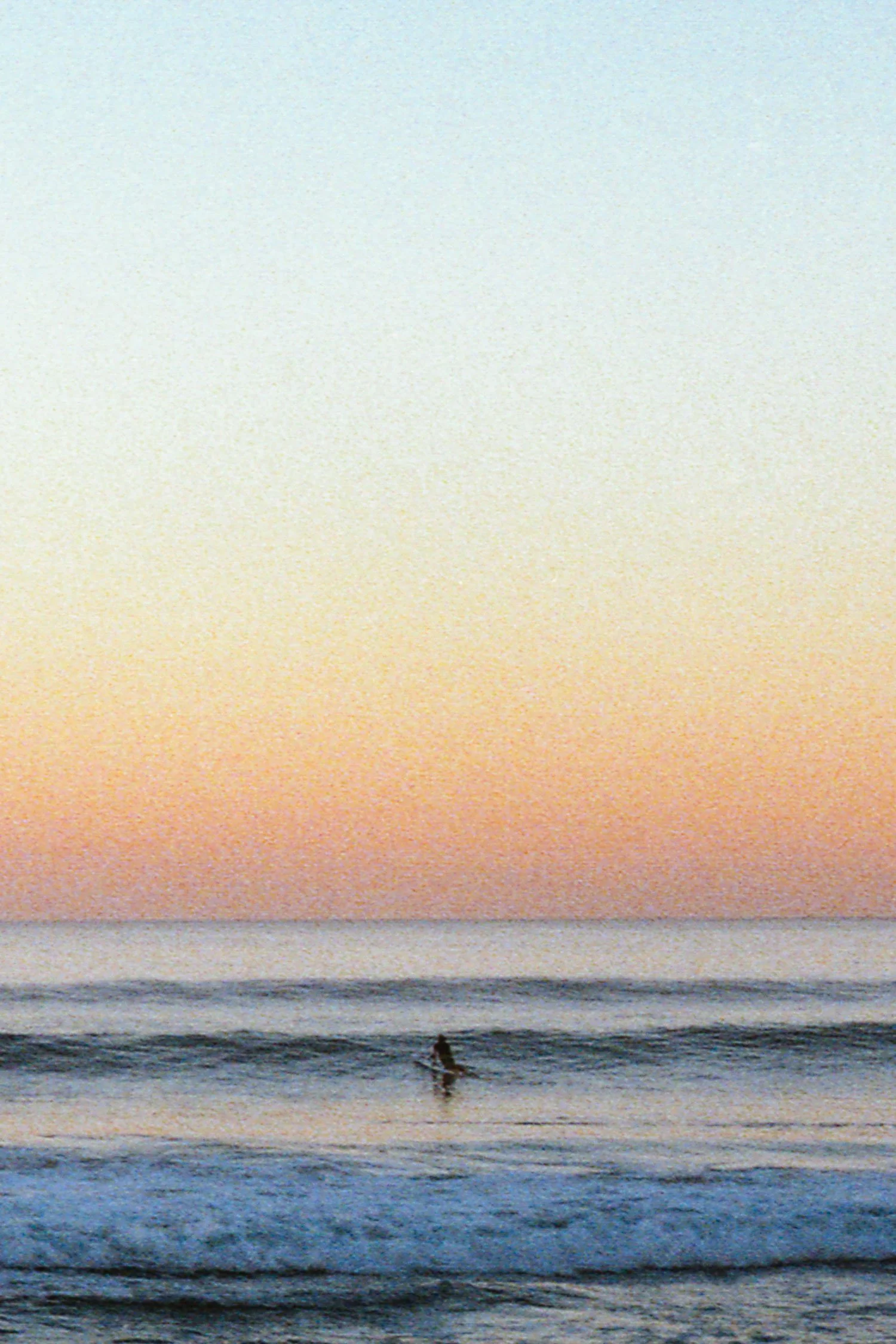 Fine art photograph of a lone surfer at sunset in Watergate Bay, Cornwall, shot on 35mm film by Karl Mackie.
