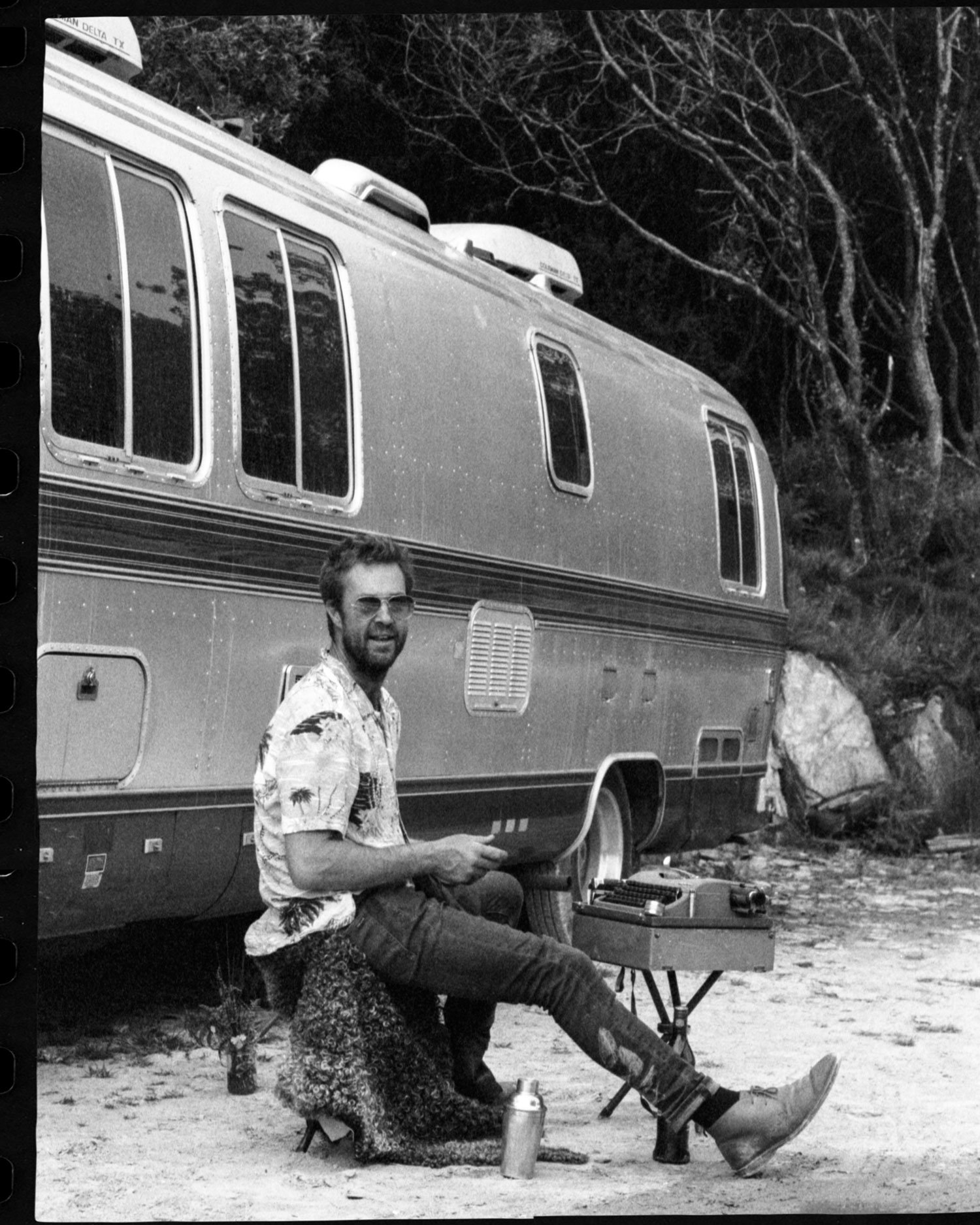 Black and white 35mm film portrait of man sitting beside vintage Airstream trailer, analogue lifestyle photography by Karl Mackie
