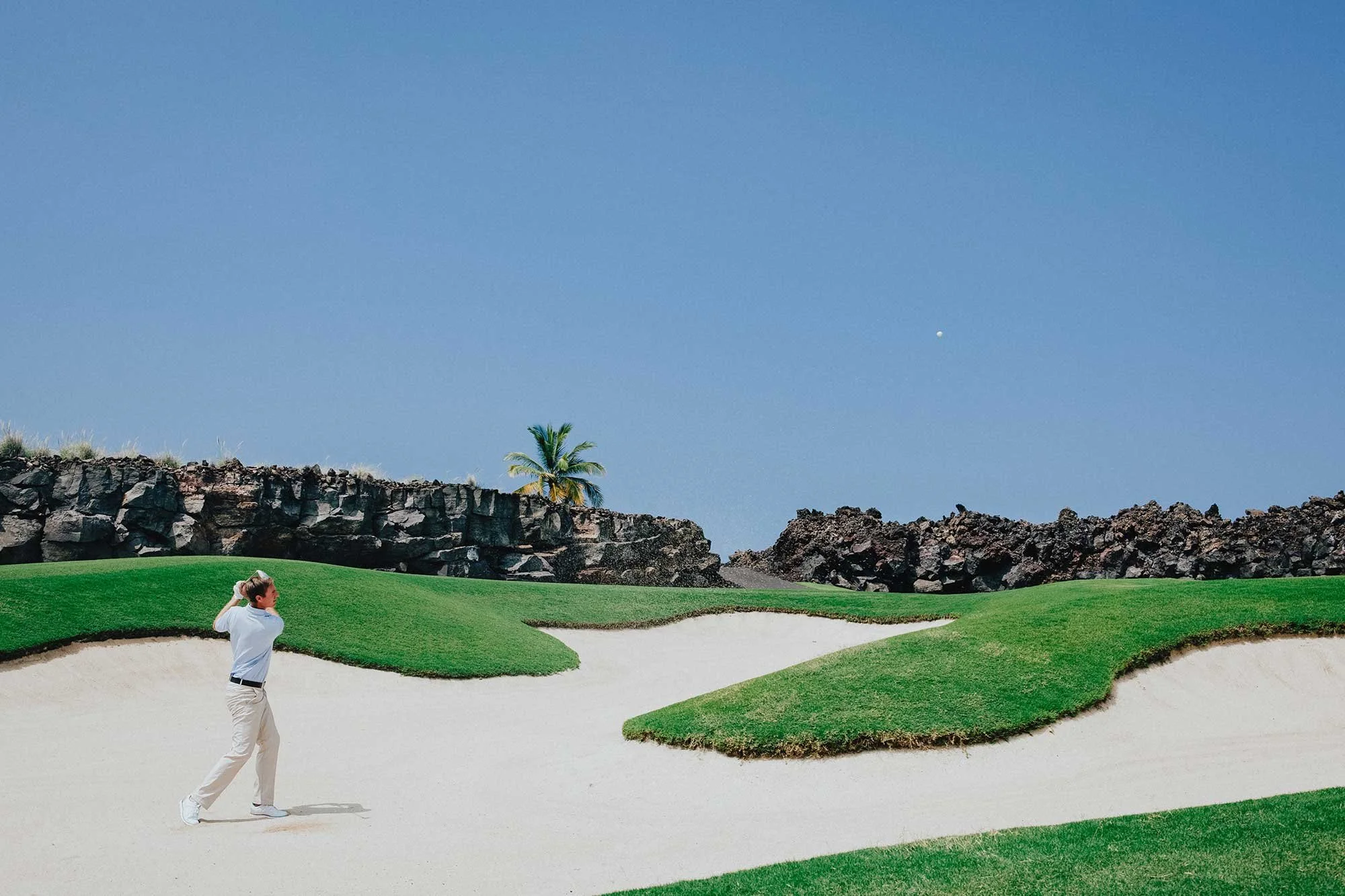 Golfer walking through a bright sculpted bunker landscape