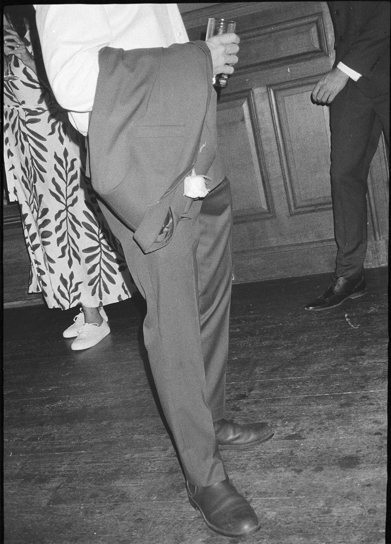 Black and white editorial film photograph of wedding guests standing at bar during reception, analogue documentary work by Karl Mackie