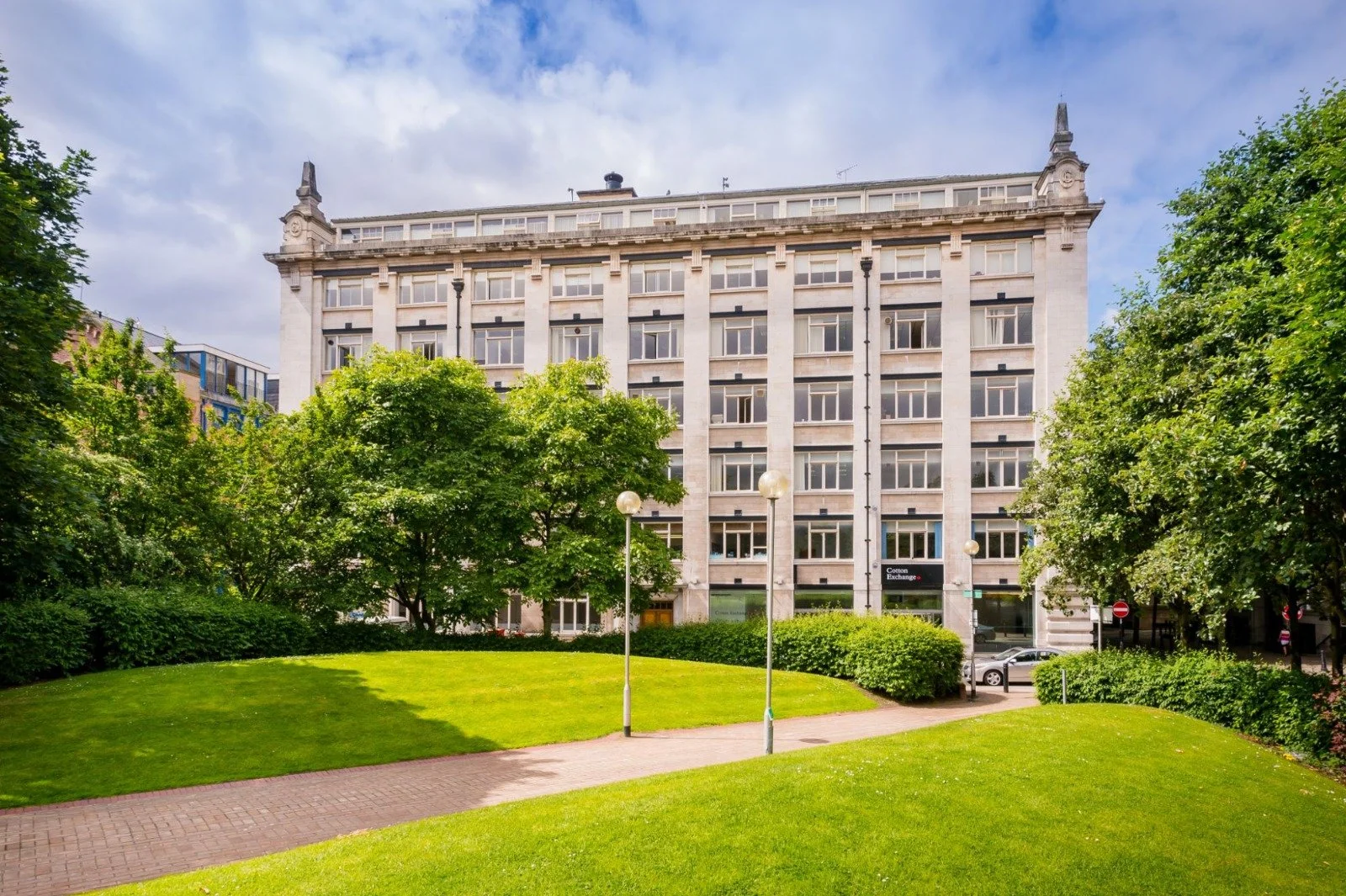 A multi-story office building with large windows, surrounded by green trees and a well-maintained lawn, on a partly cloudy day.