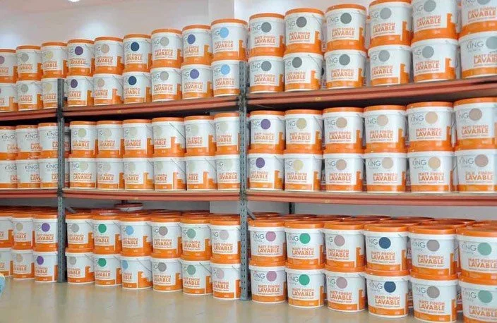 Étendue de plusieurs rangées de bidons de peinture ou de produit en grande quantité, stockés sur des étagères dans un entrepôt ou un magasin.