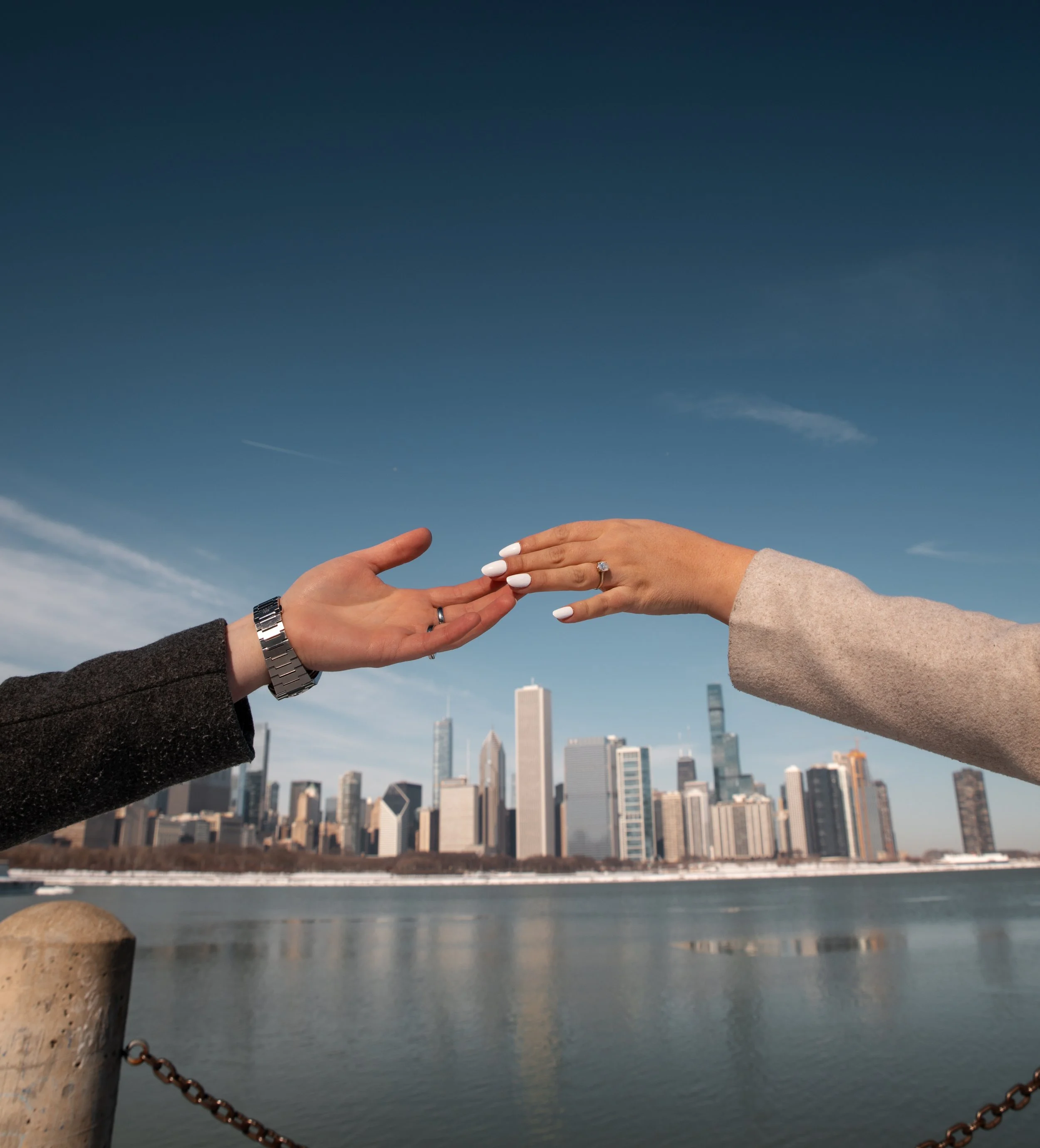 Two hands reaching towards each other against a city skyline and river background.