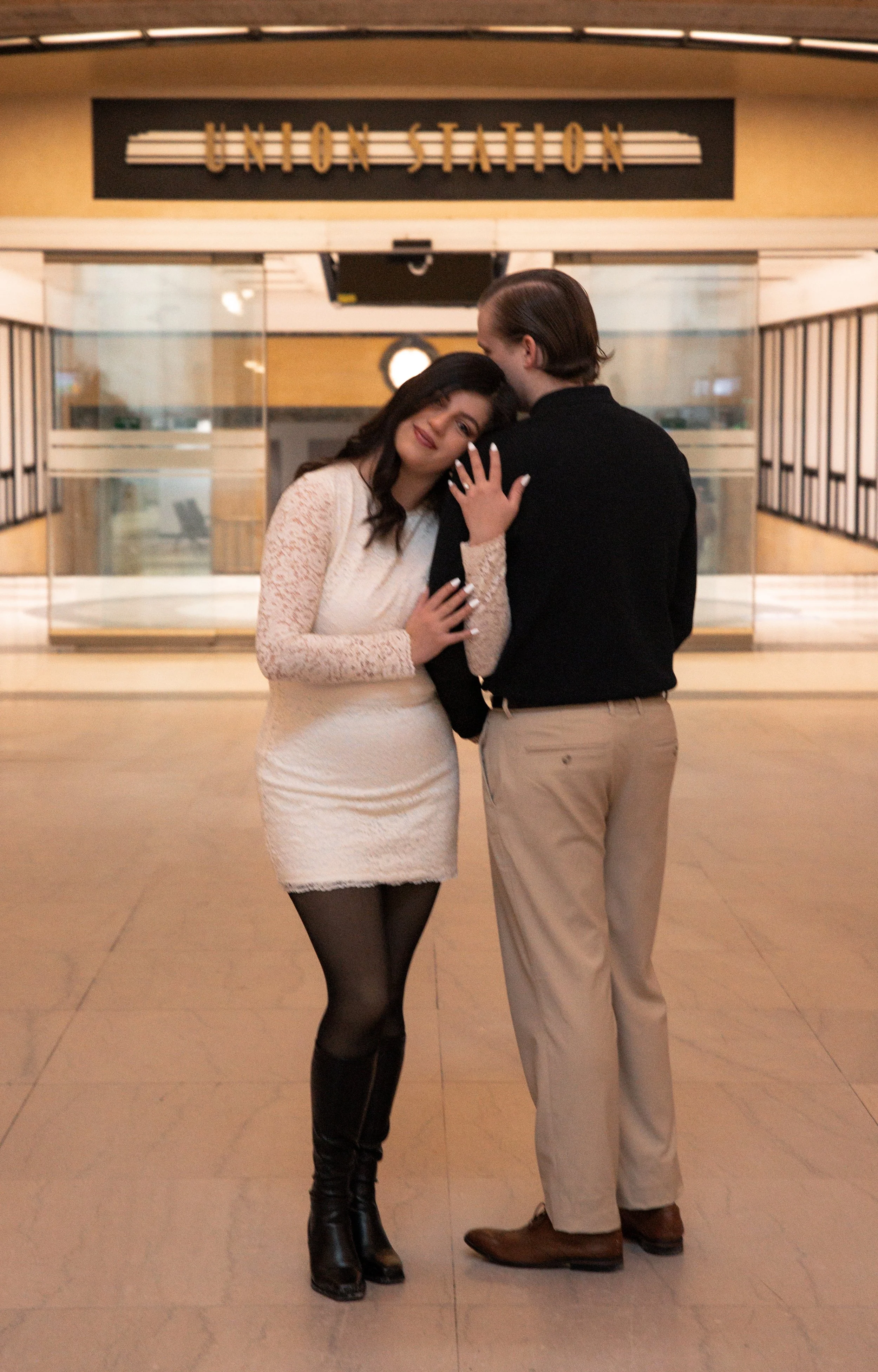 A man and woman embracing in a train station with a sign reading 'Union Station' above them.