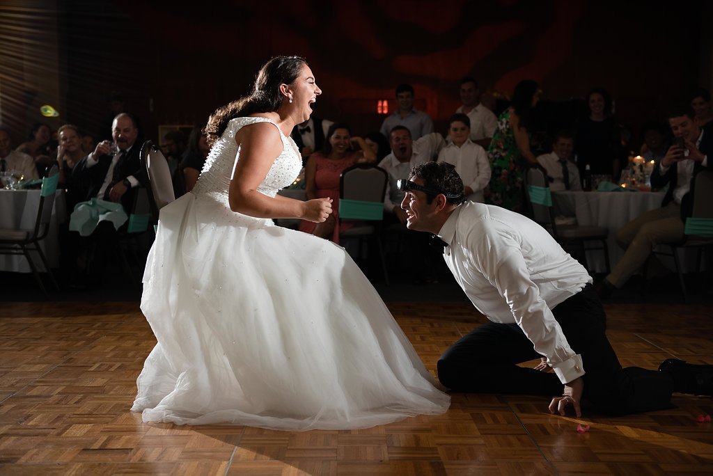 Bride and groom in playful dance on reception floor with guests watching.
