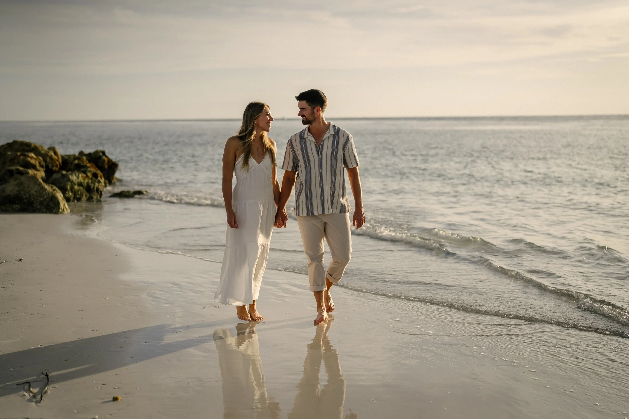 A couple walking hand-in-hand along the beach at sunset.