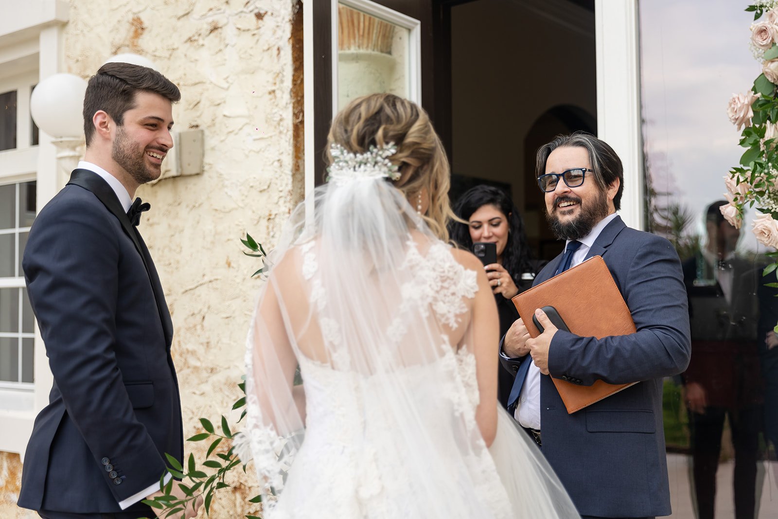 Bride and groom at wedding ceremony with officiant and guest, smiling.