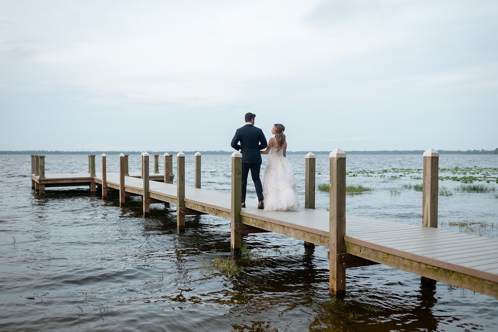 Bride and groom standing on a wooden dock overlooking a lake.