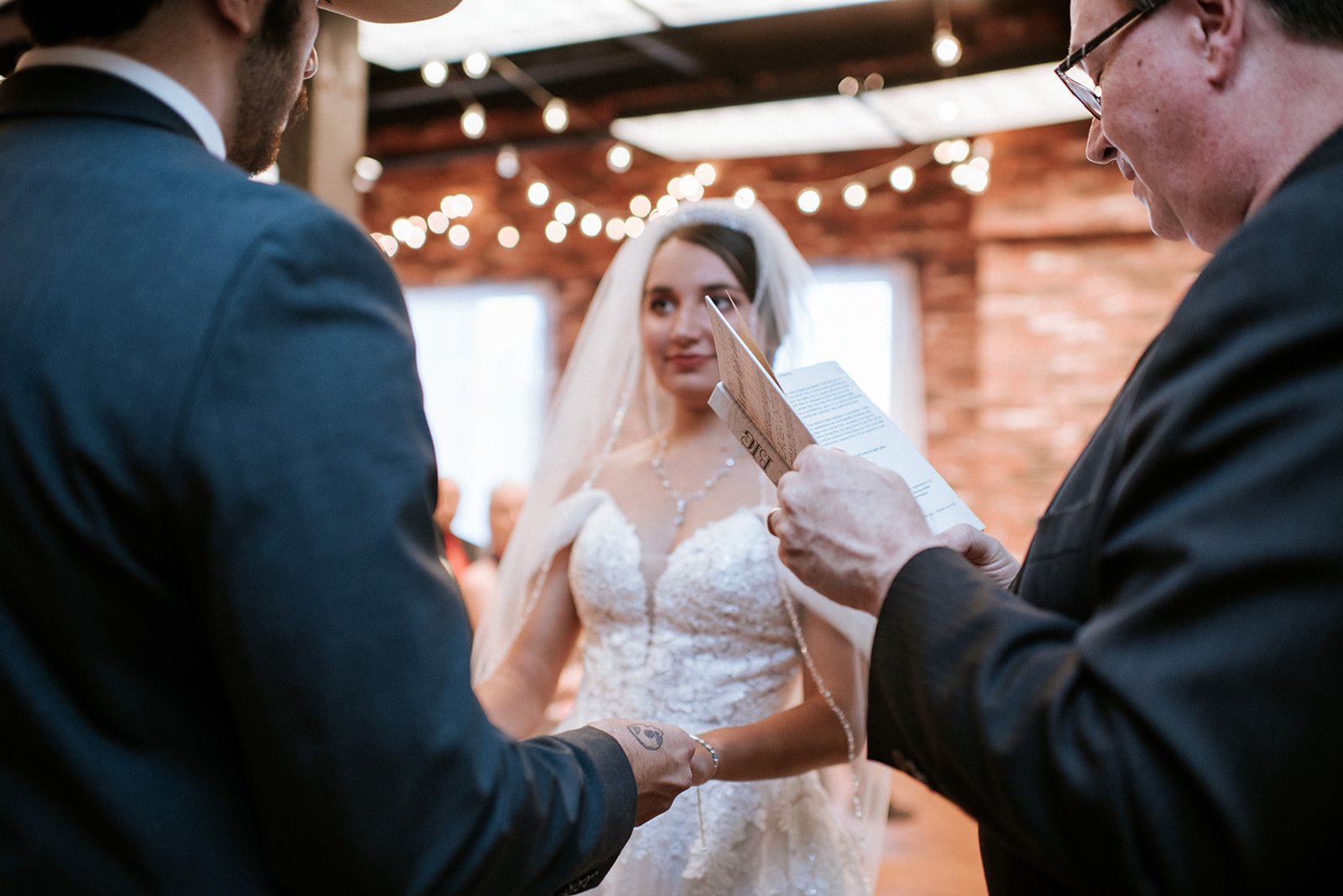 Bride and groom during a wedding ceremony with an officiant, indoors with string lights.