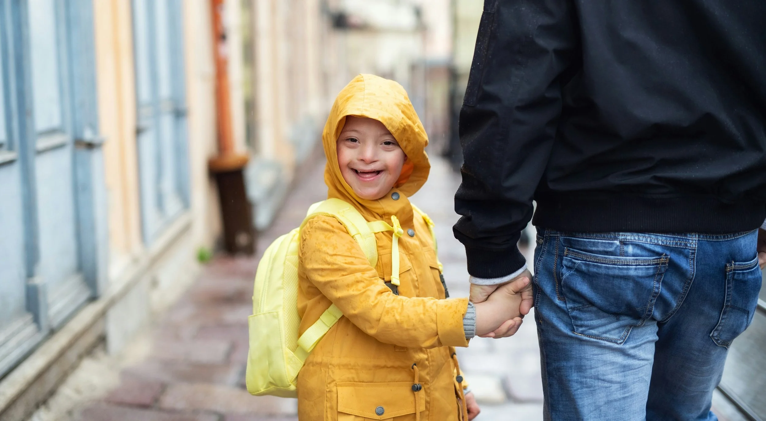 Down syndrome boy in yellow raincoat holding man’s hand