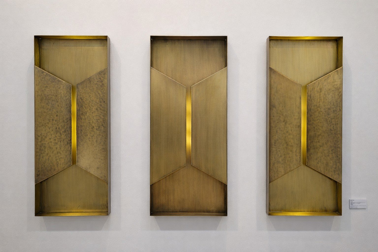 Three sculptural wall sconces in patinated bronze with a polished brass light line, AmorettiLAB