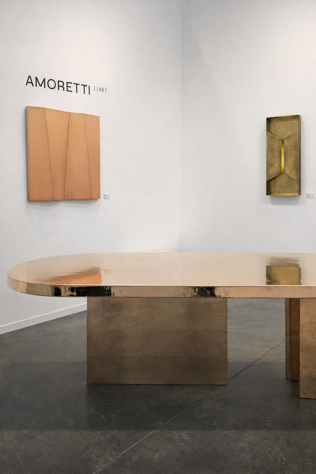 An art gallery with two abstract art pieces on a white wall and a shiny metallic table in the foreground.