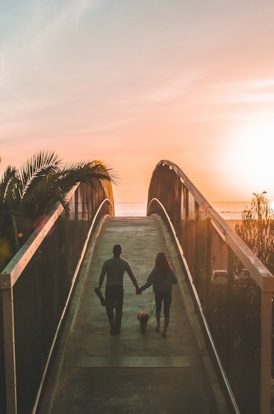 A couple walking over a bridge, into the sunset