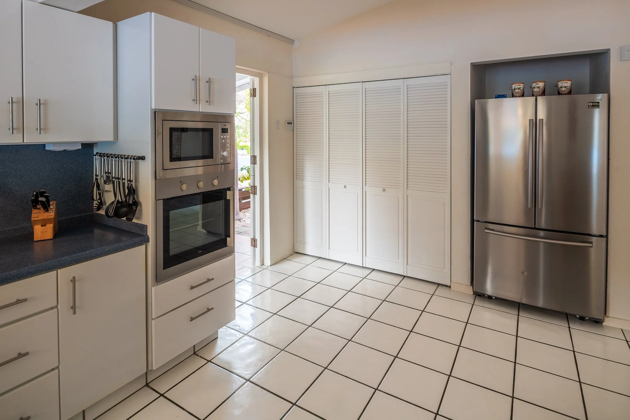 Kitchen with white cabinets, black countertops, a microwave, oven, and stainless steel refrigerator, with tiled floor.