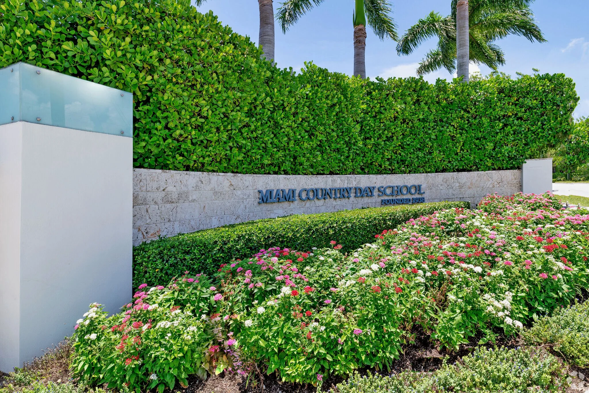 Entrance sign of Miami Country Day School surrounded by greenery and colorful flowers.