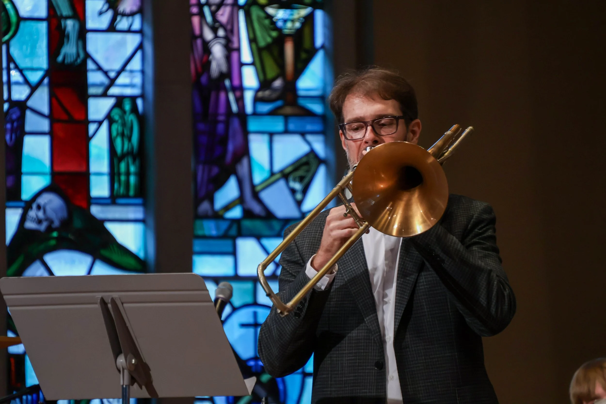 Dr. Benjamin Yates plays trombone for Festival Band concert in Boe Chapel with stained glass behind his head