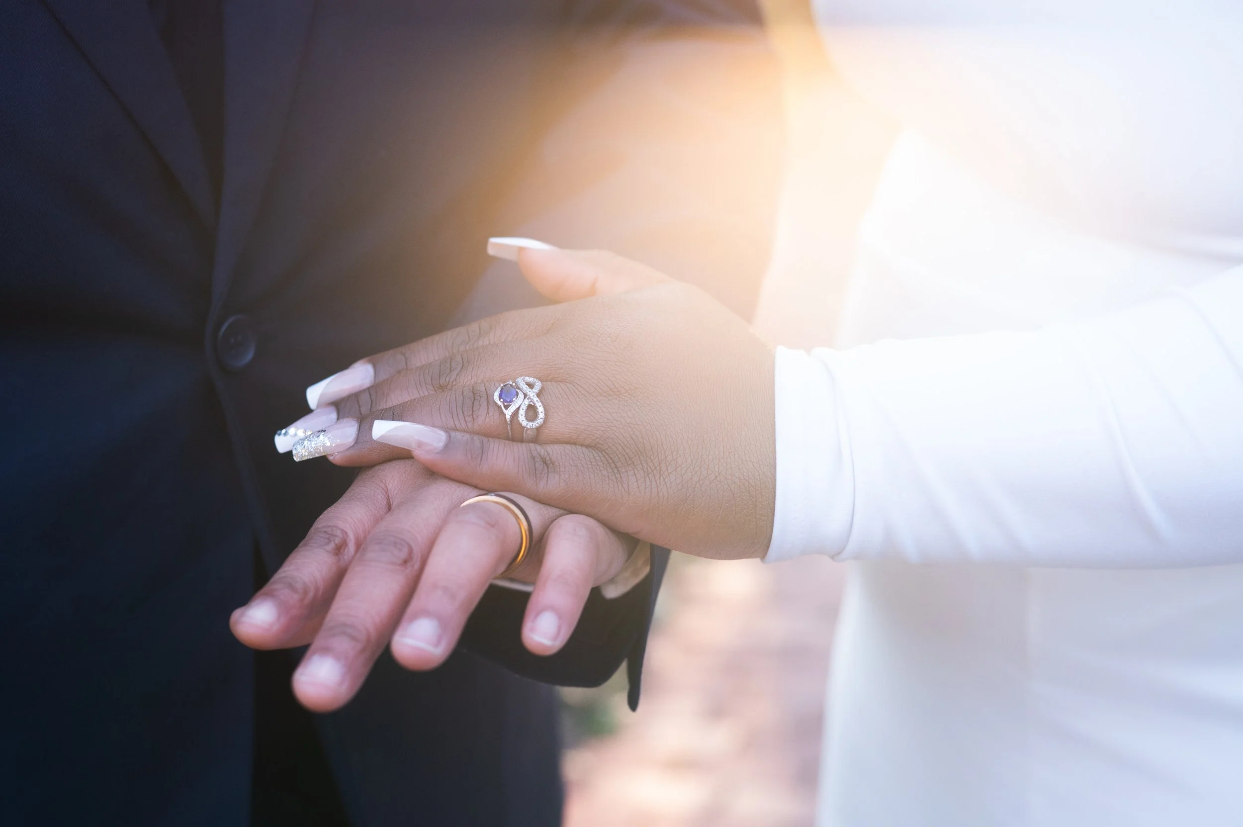 Two women hold their hands flat on top of each other showing off their wedding bands as a ray of sunlight shines over them from above. 