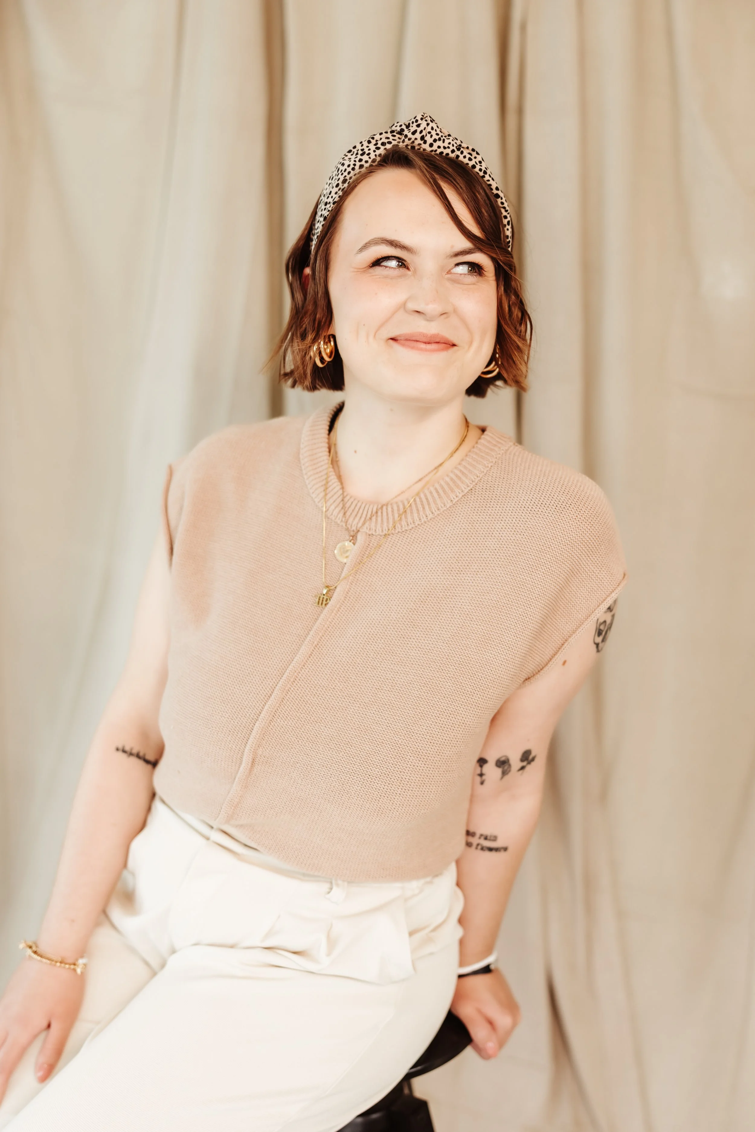 A woman looking off to the right smiling sitting on a stool