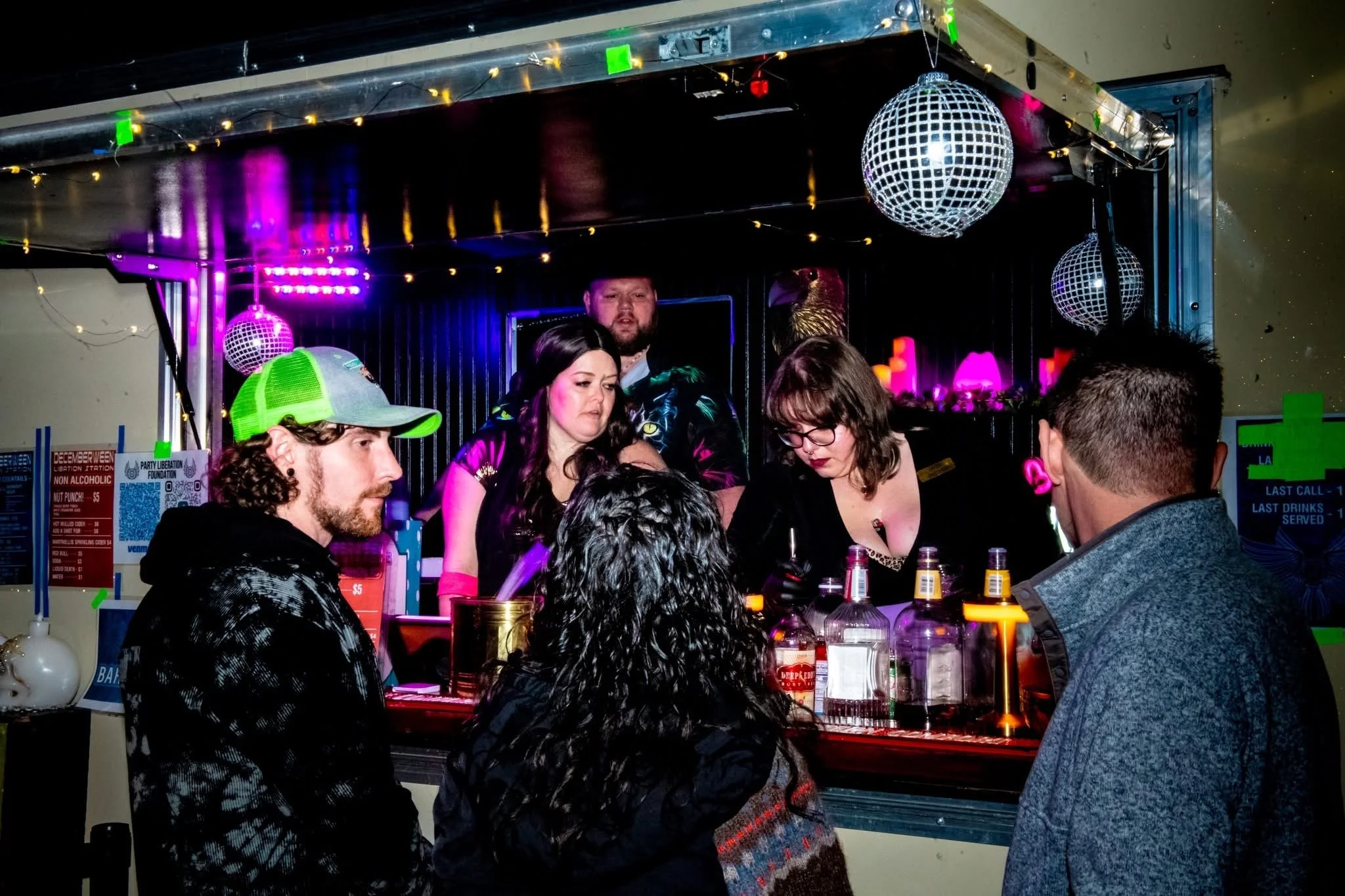 People at a bar with DJs, disco balls, and colorful lights.