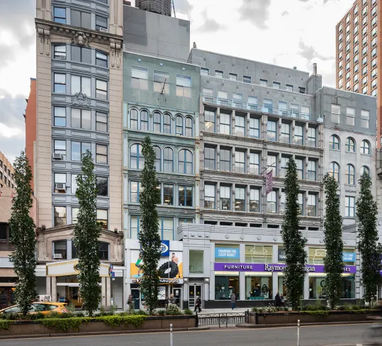 City street with tall buildings, trees, and pedestrians.