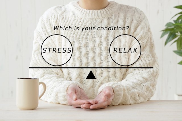 A person in a white, cable-knit sweater sitting at a table with a beige mug, with a balance scale graphic overlay asking 'Which is your condition?' with options 'Stress' and 'Relax'.