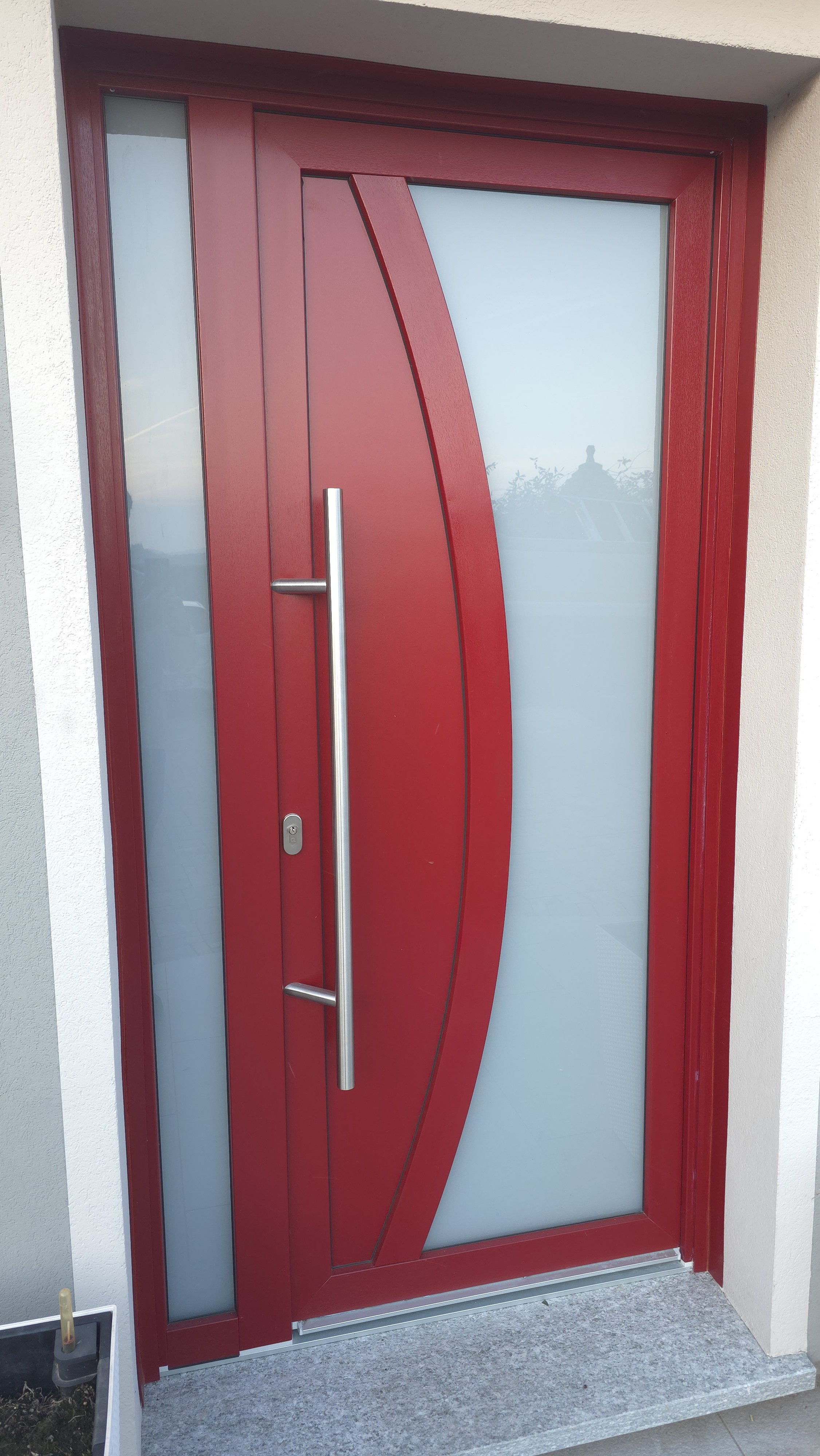 Porta di casa moderna di colore rosso con vetro opaco e maniglia lunga in metallo.
