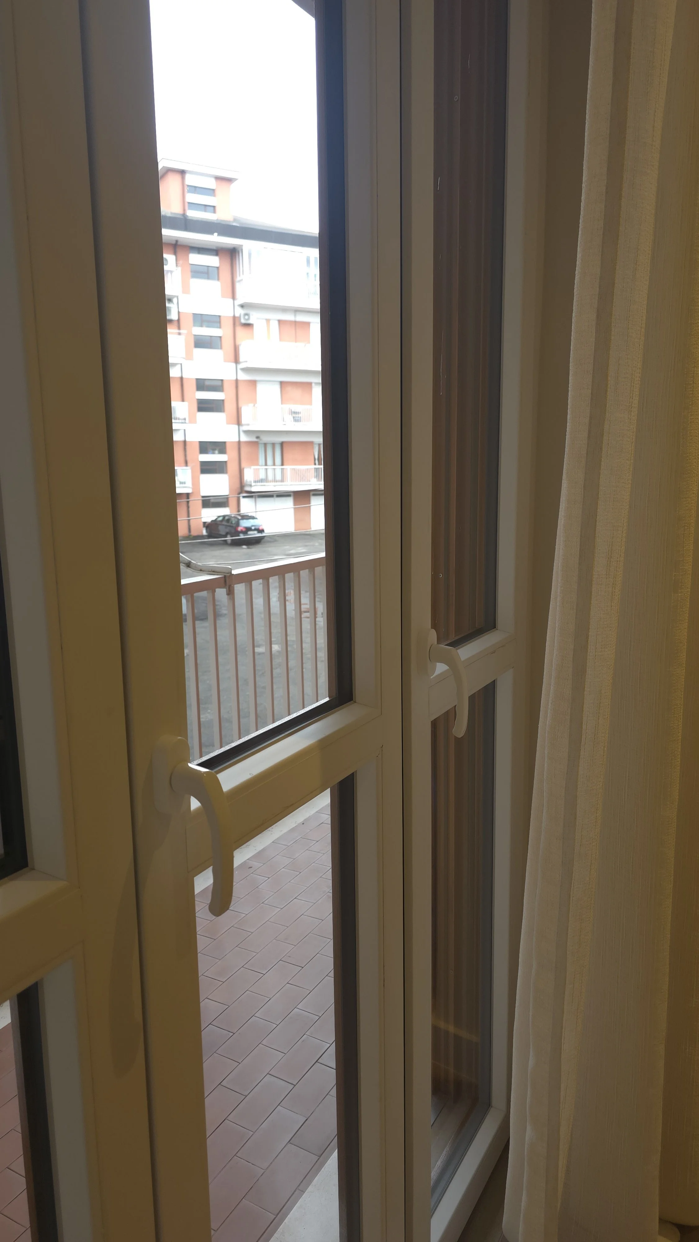 Vista da una finestra con vetri doppi, parapetto e un edificio residenziale che si vede sullo sfondo.