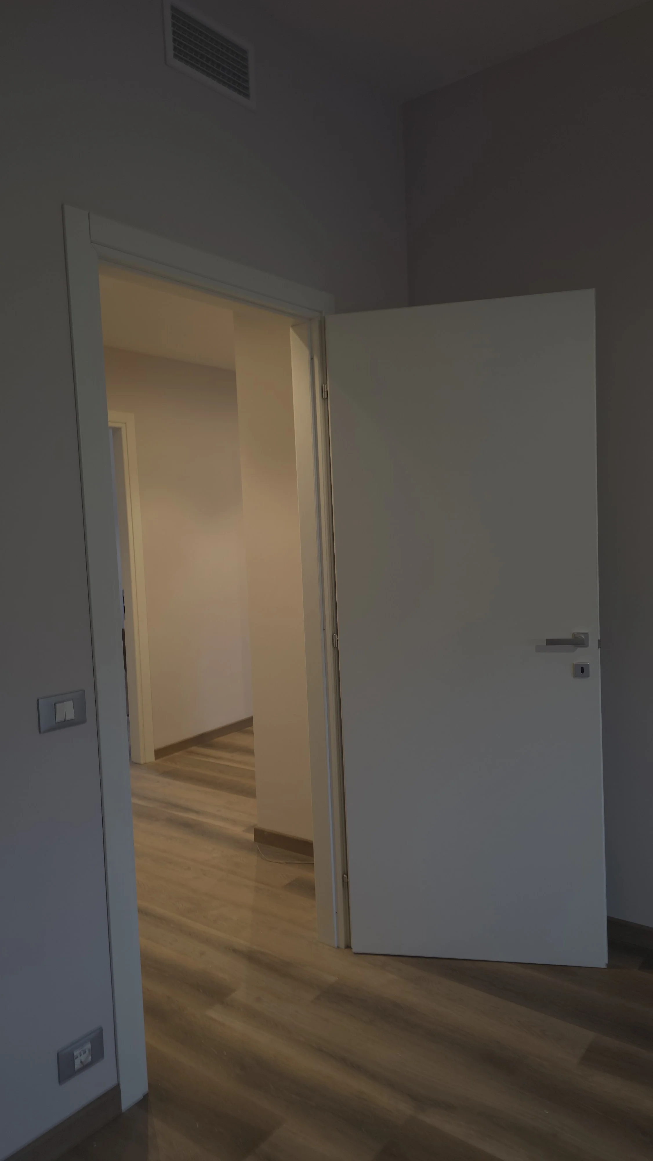 Porta aperta che conduce a un corridoio con pavimento in legno e pareti bianche.