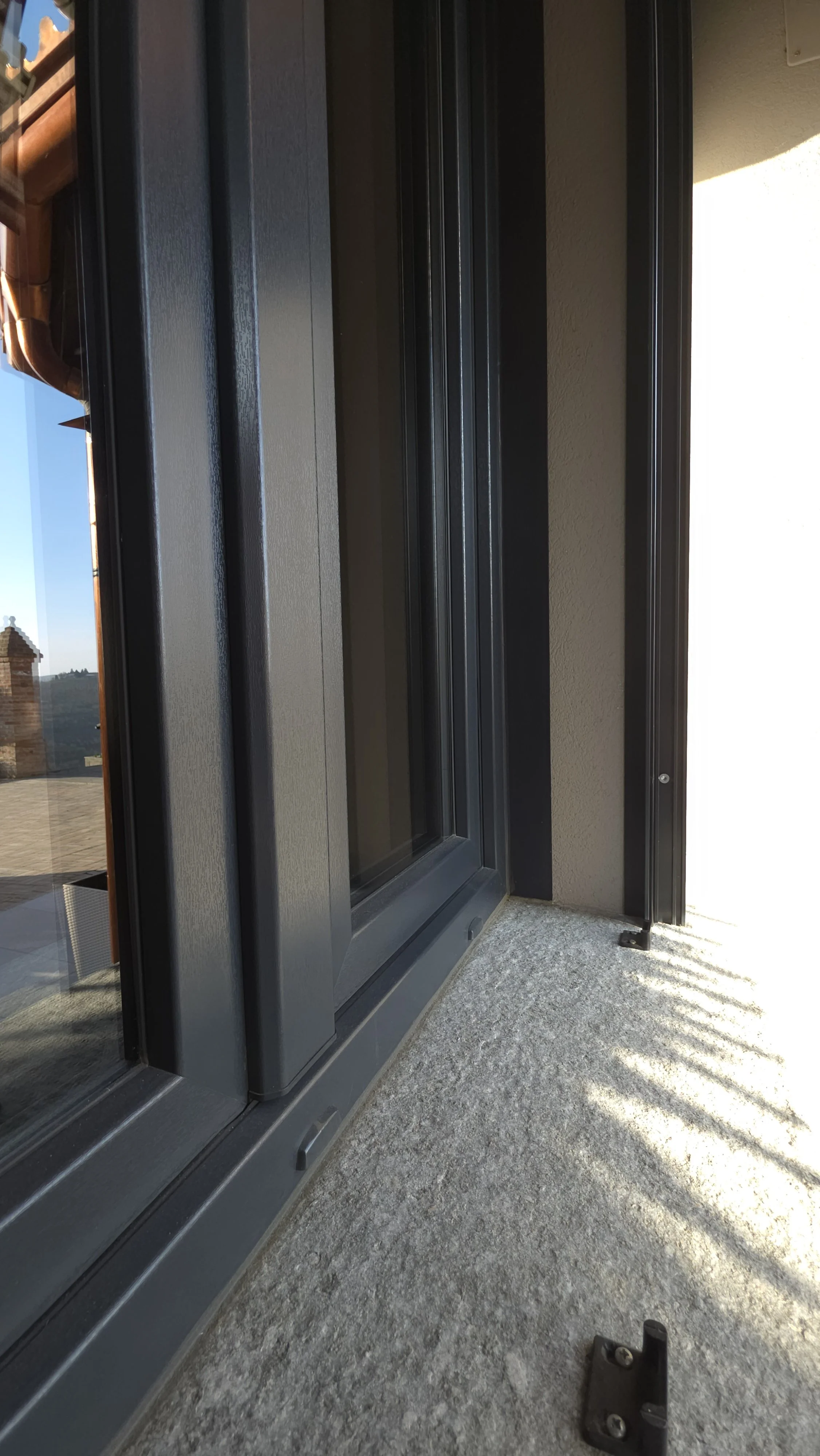 Dettaglio di una finestra moderna con discussa oscurata e battuta aperta su un balcone con pavimentazione in cemento.