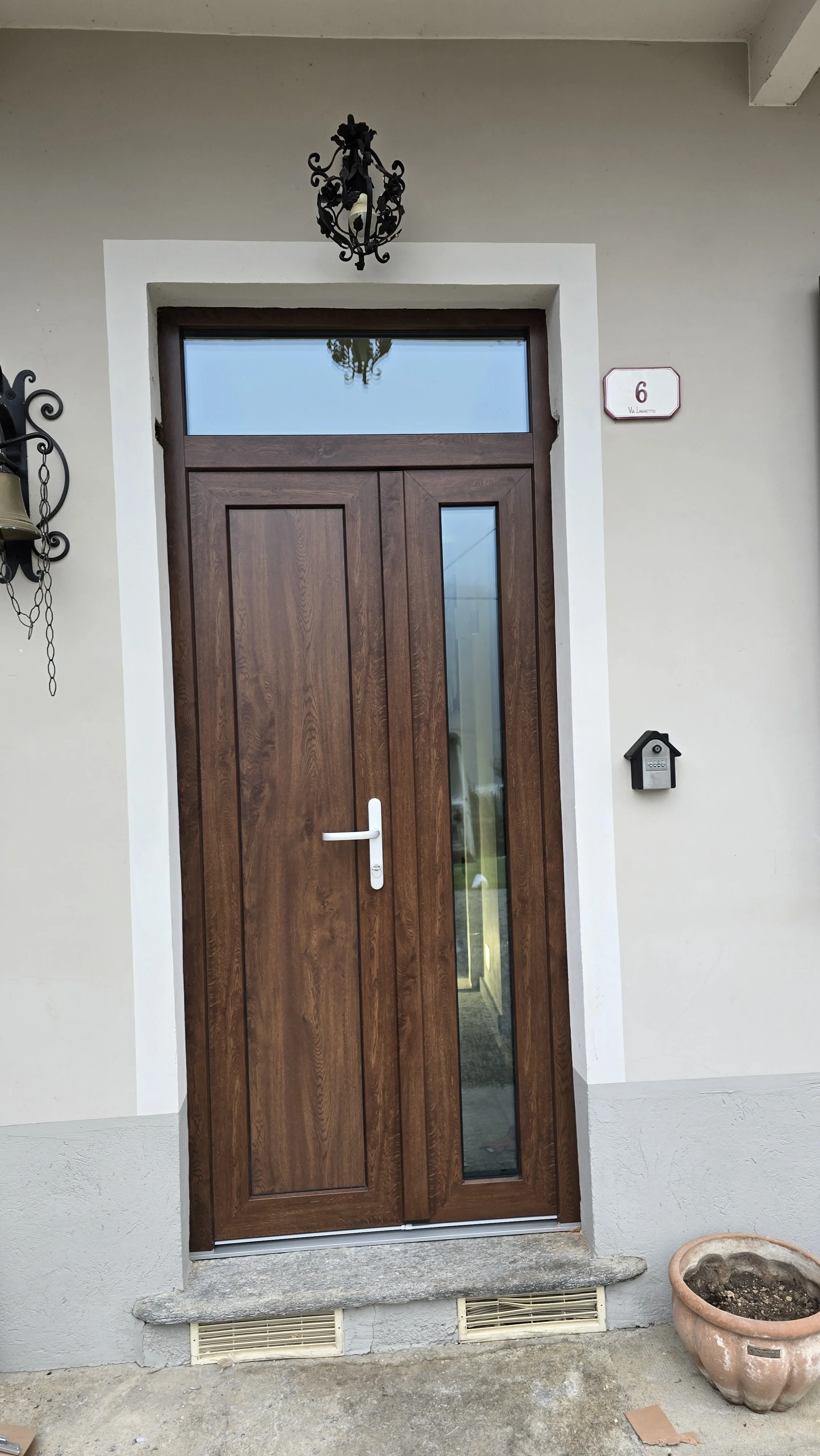 Porta d'ingresso in legno con vetro, illuminata da una lampada in ferro battuto sopra.