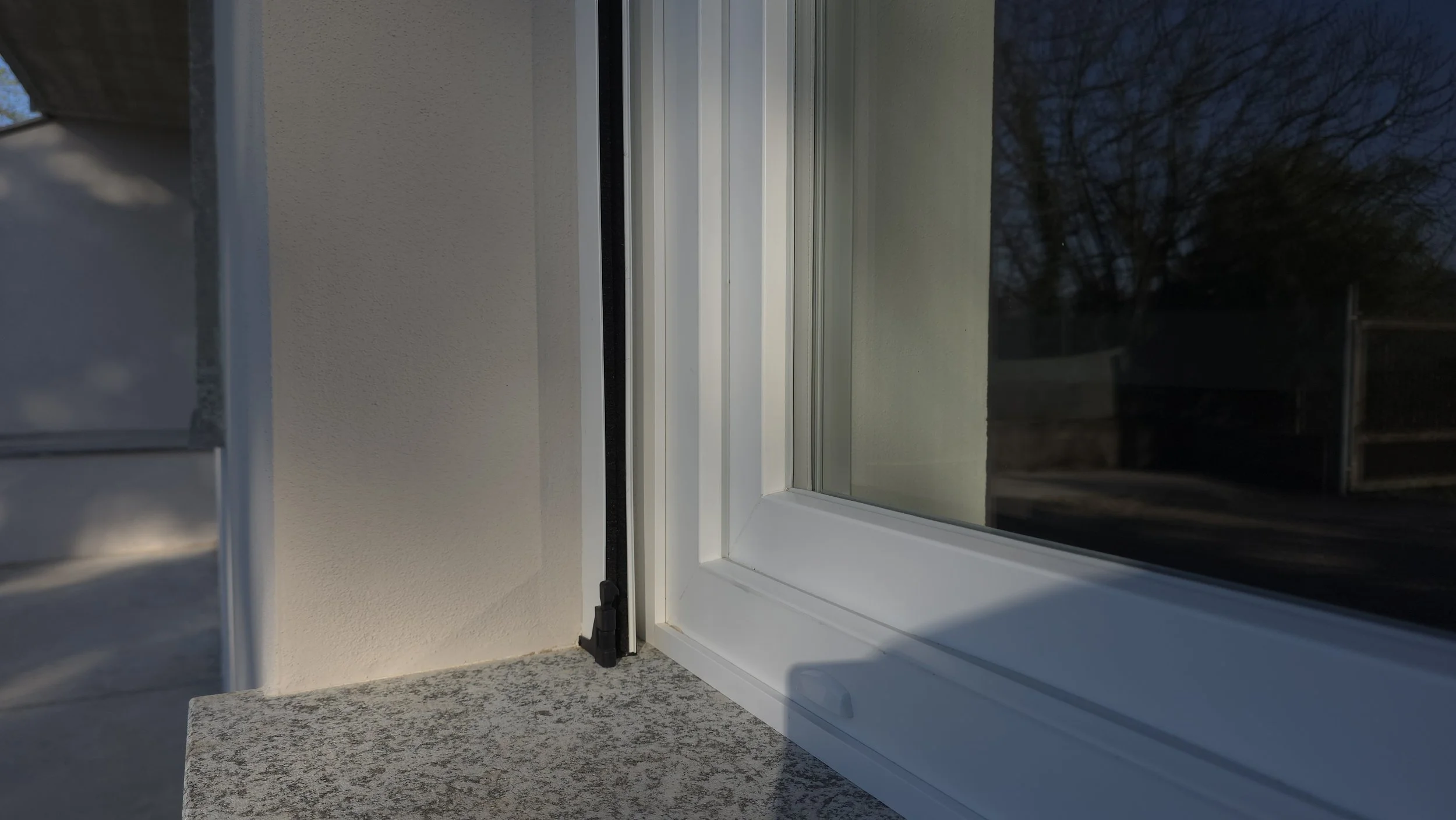 Una finestra in PVC bianco con una cornice e un davanzale in granito, rubata alle prime luci del mattino