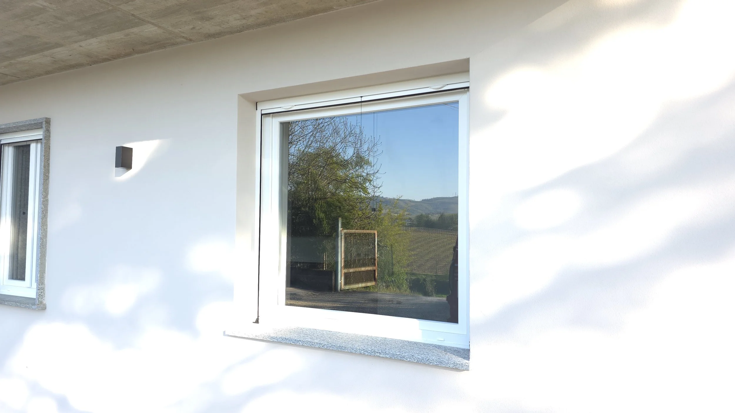 Finestra grande con scorrevole sulla facciata di un edificio, con vista sul paesaggio collinare e albero vicino.