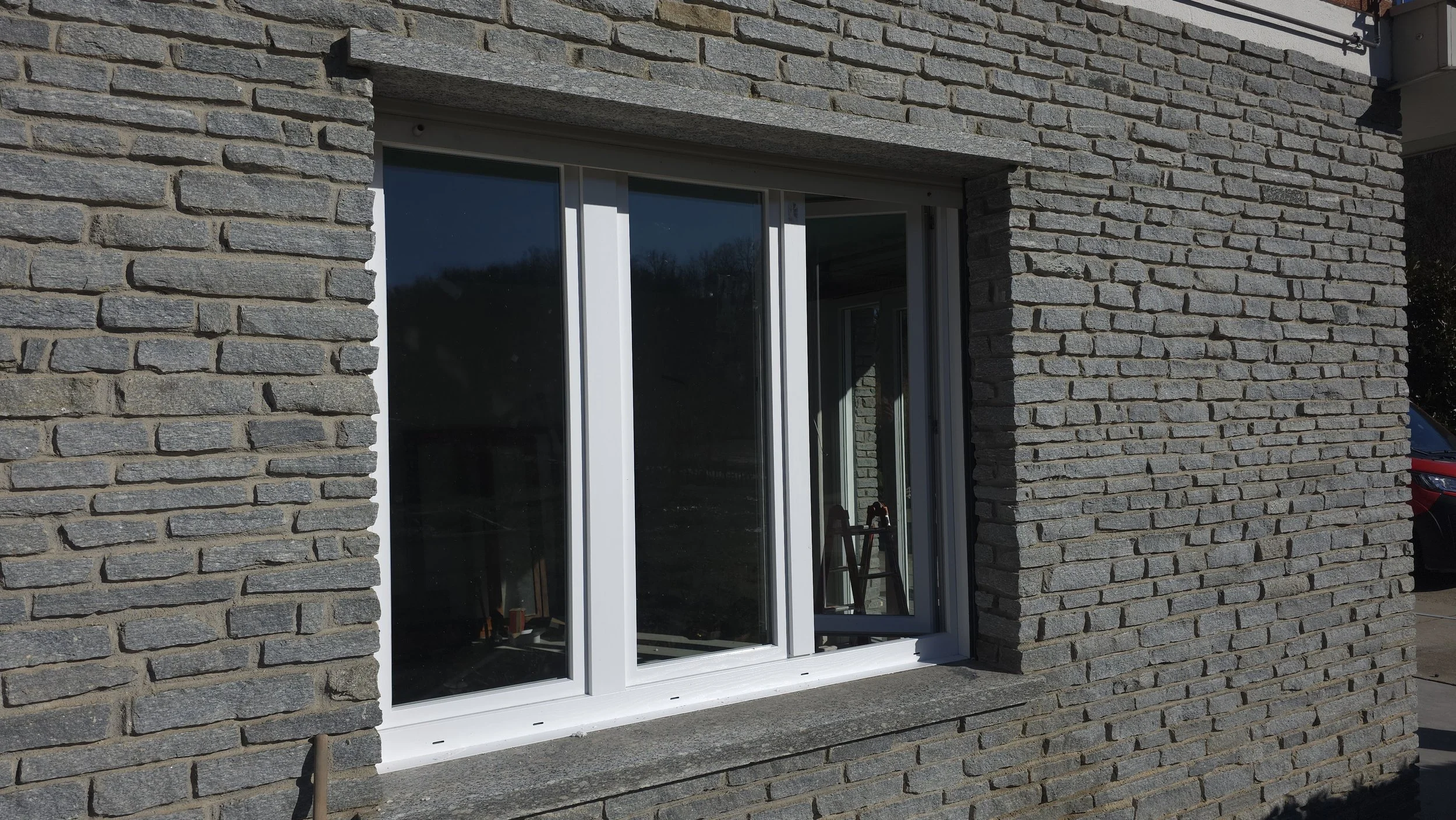 Finestra con struttura bianca inserita in un muro di pietra grigia a muro a vista