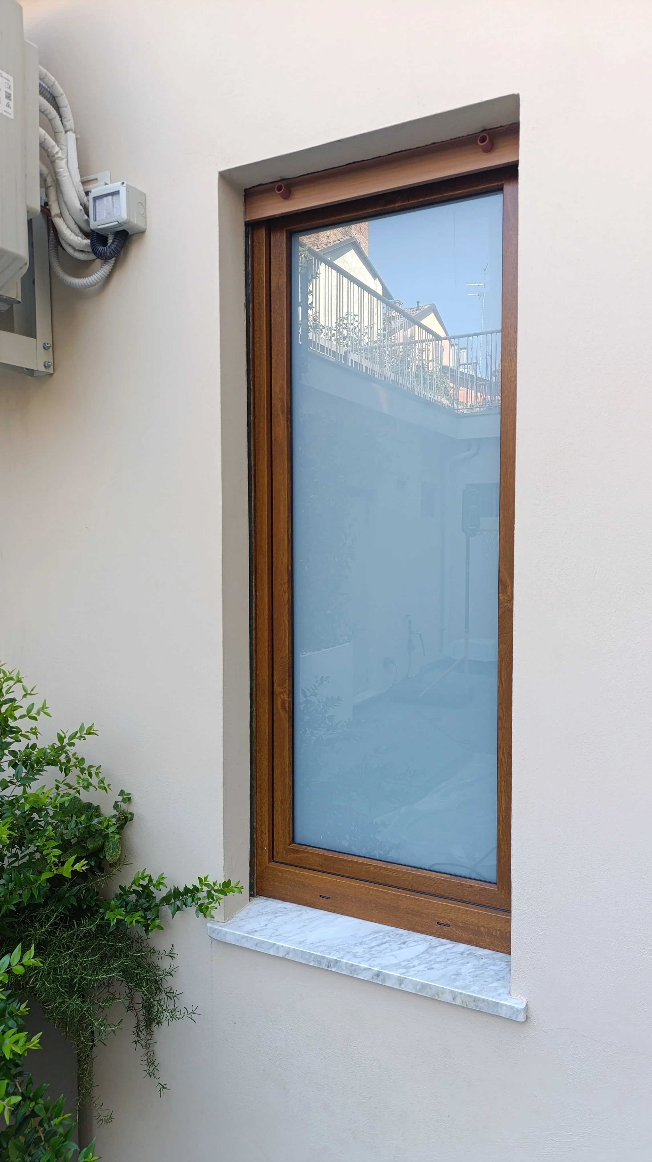 Finestra con cornice di legno sulla parete di un edificio, riflette il cielo e un balcone con ringhiera in metallo