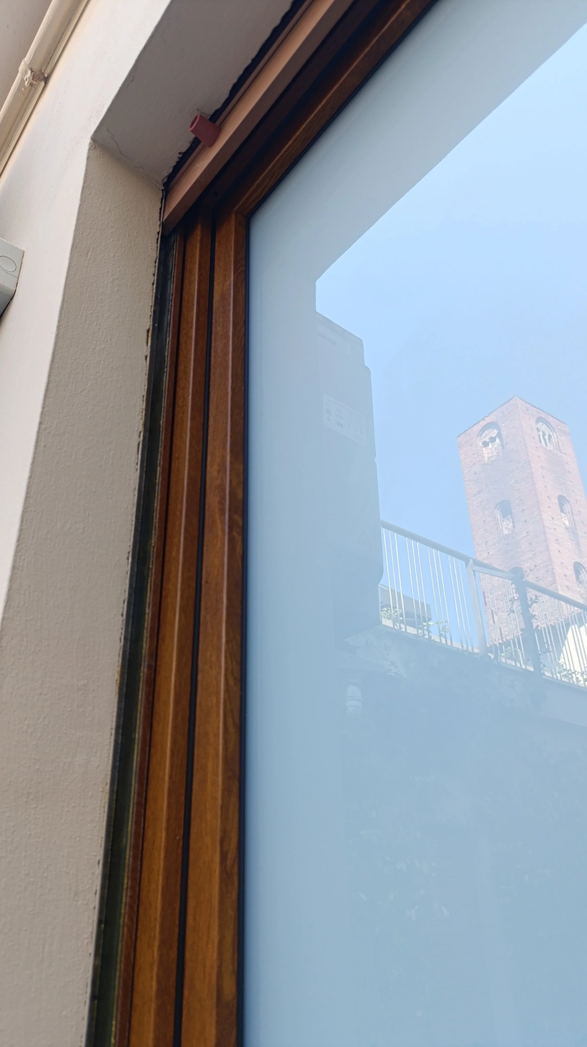 Finestra con doppio vetro, vista di un campanile in pietra in lontanza con cielo chiaro.