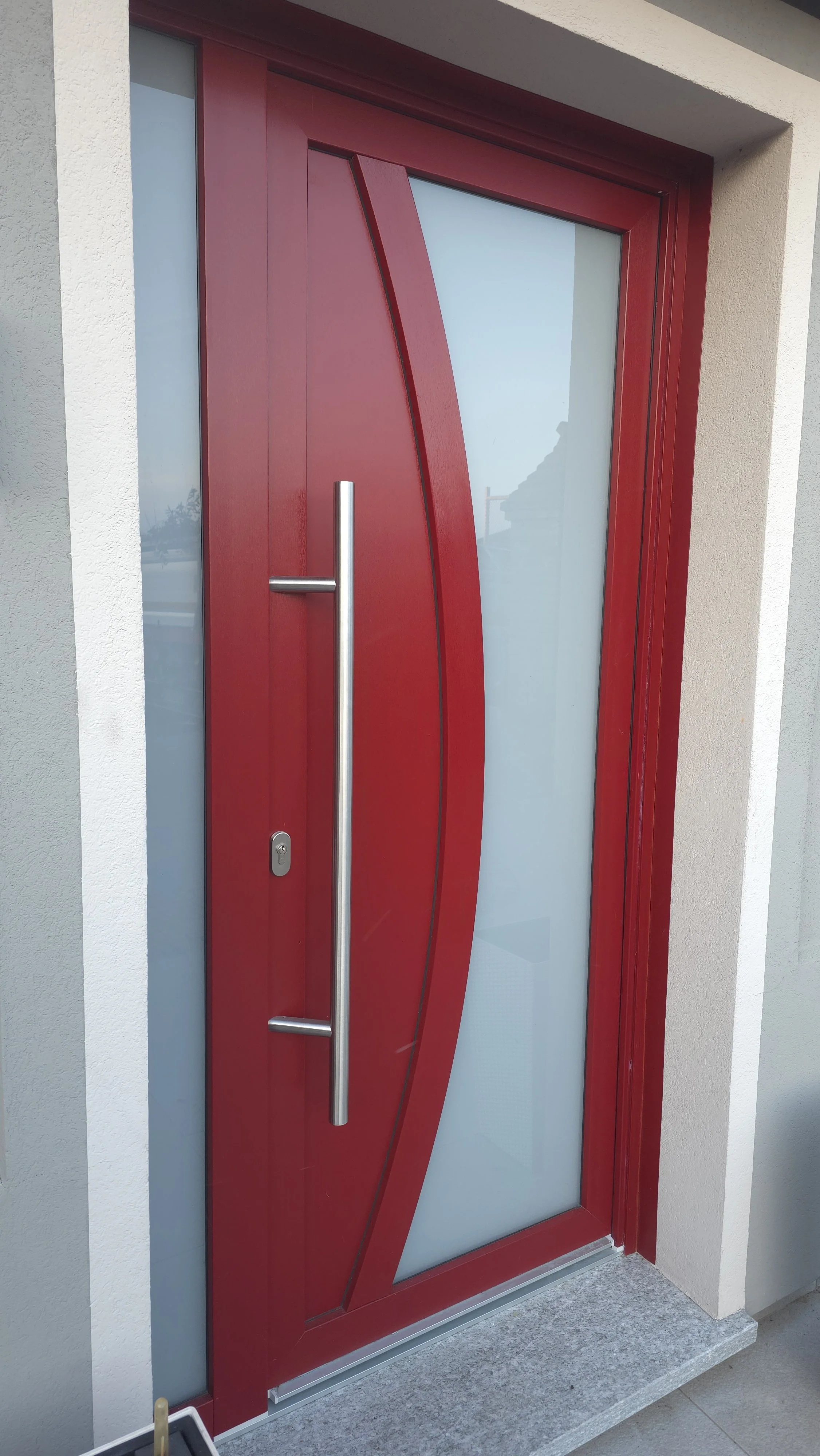 Porta d'ingresso moderna di colore rosso con finestra in vetro satinato e maniglione in metallo.