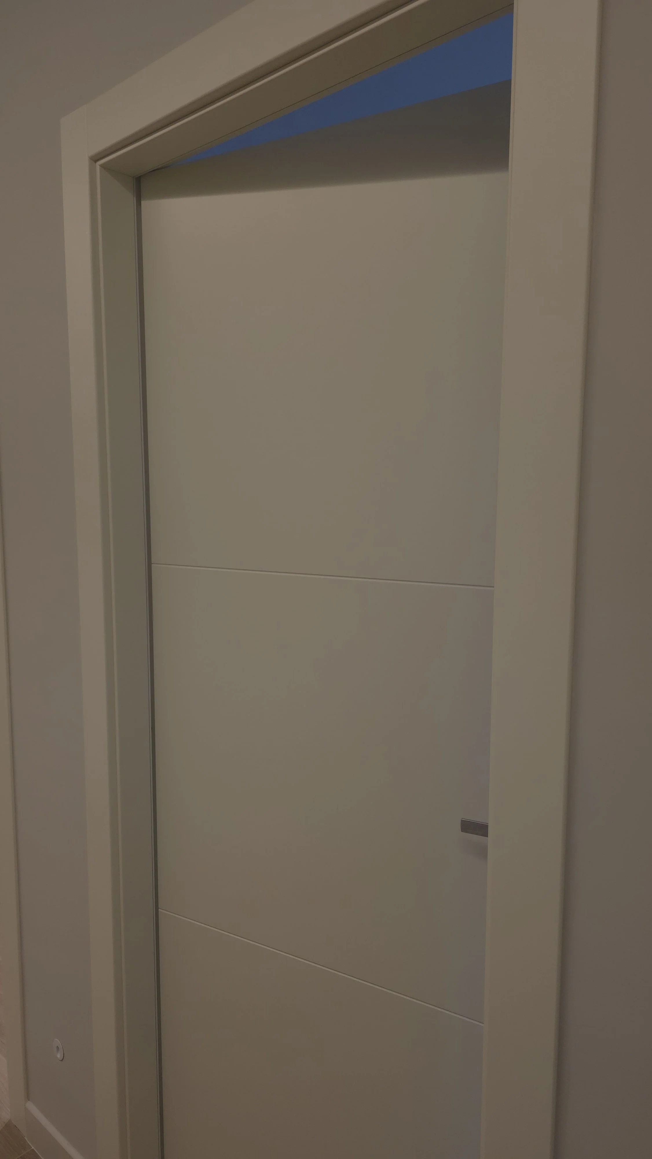 Una porta scorrevole bianca in un edificio, con un telaio bianco e una maniglia metálica, aperta su un ambiente con pareti a color crema.