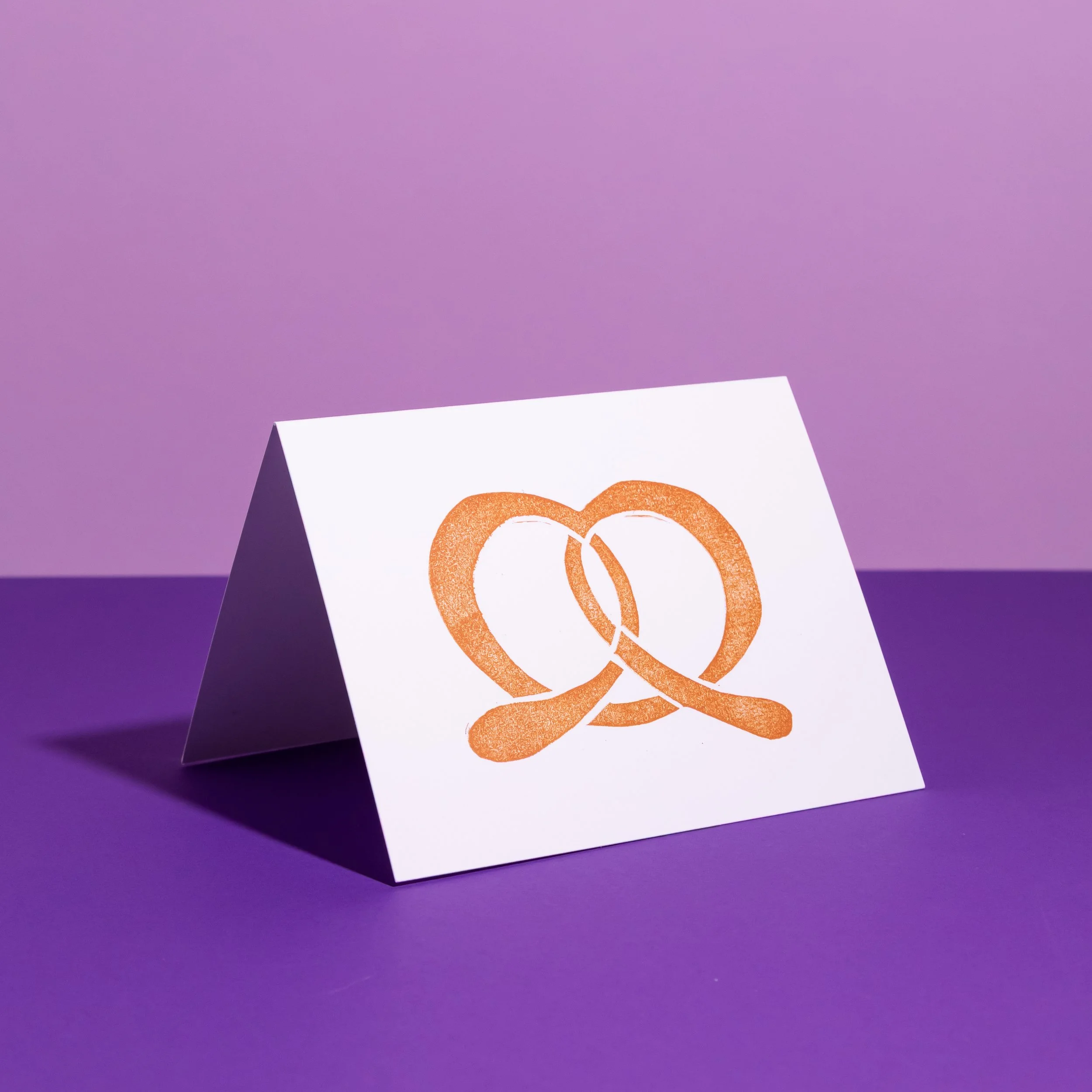 A hand-stamped linocut card featuring a pretzel. Designed by Andrea Morris Studio.