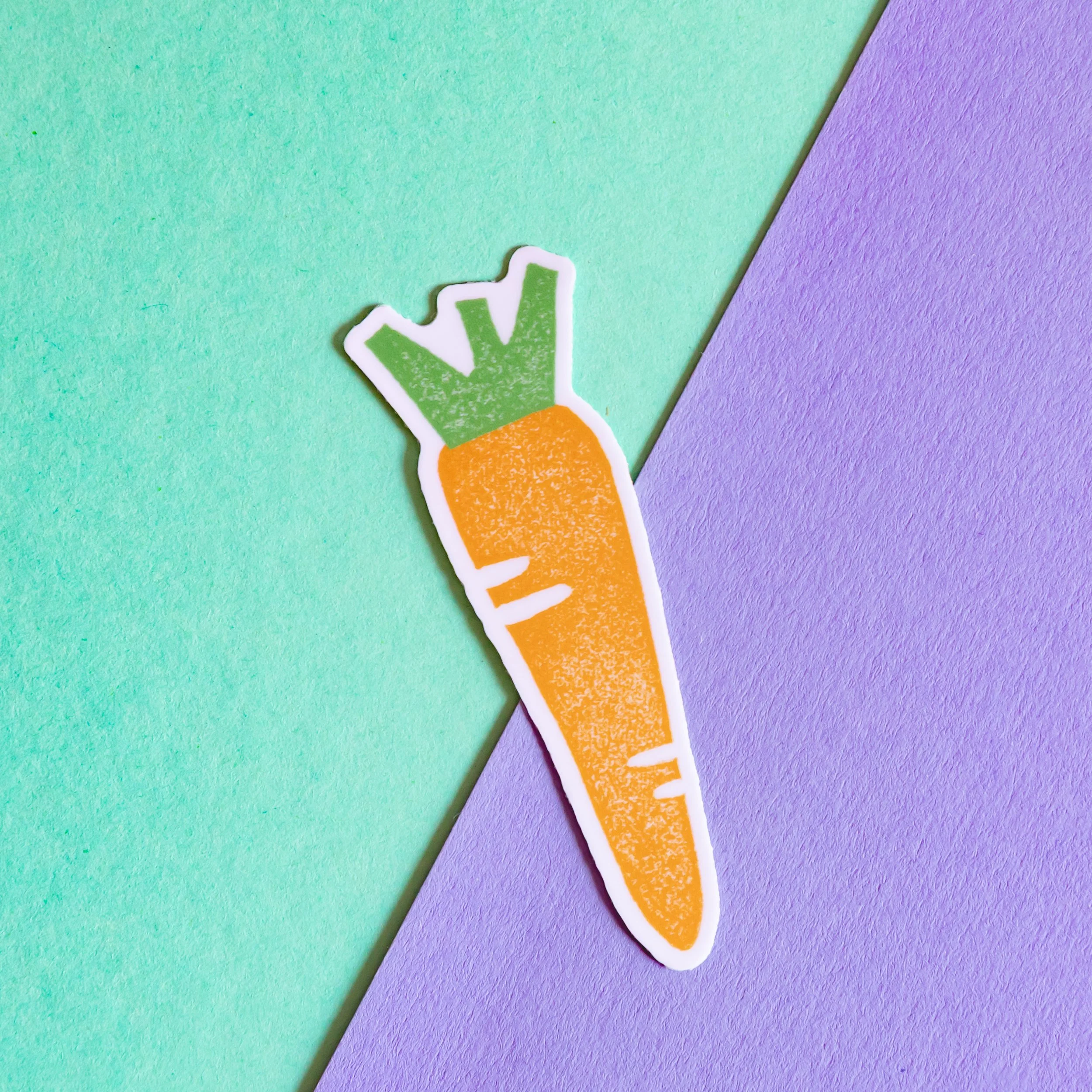 Close-up of a multicolored paper background with a sticker of a carrot with green leafy top on the purple section.