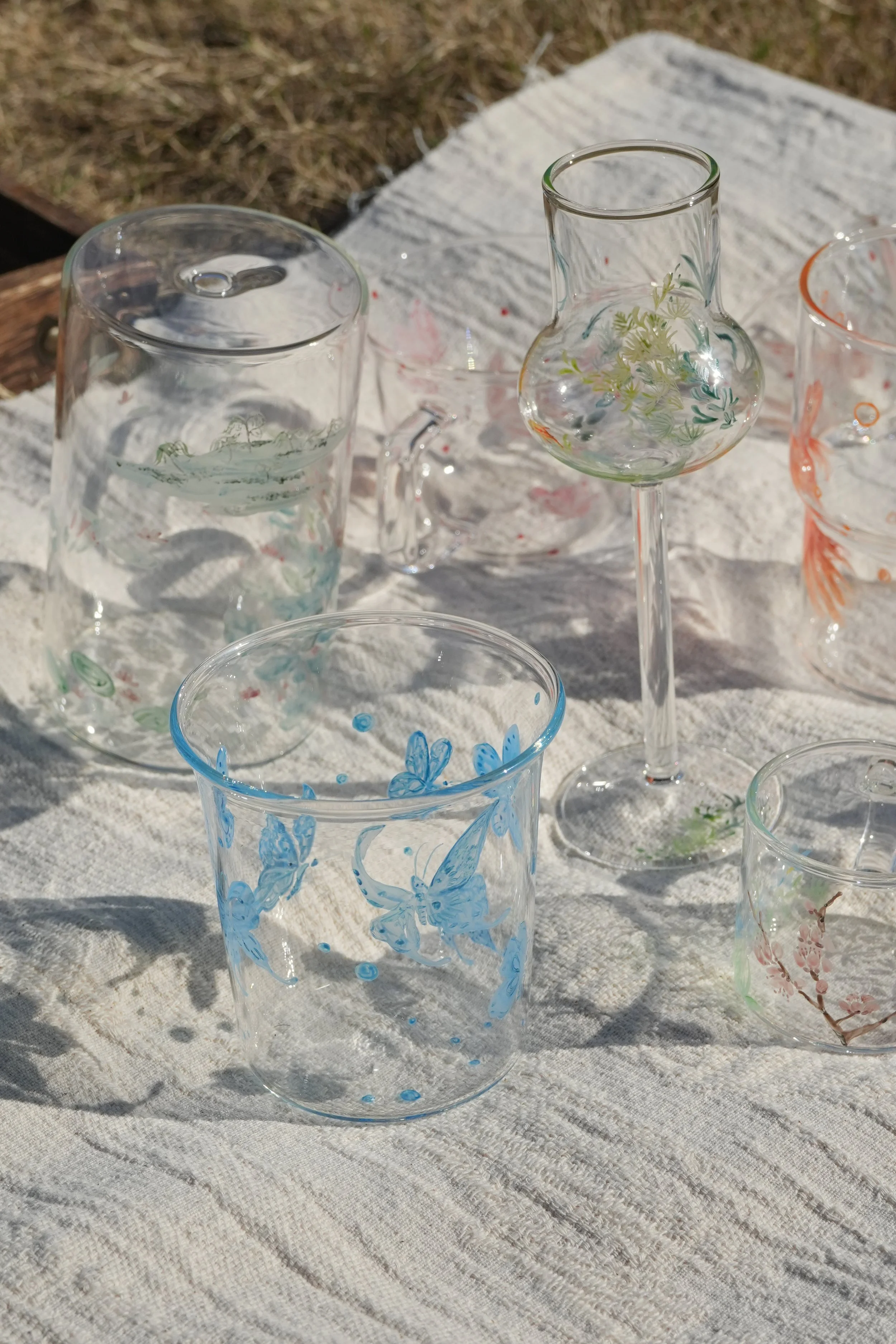 Photograph of several hand-painted glass cups laying on a white blanket.
