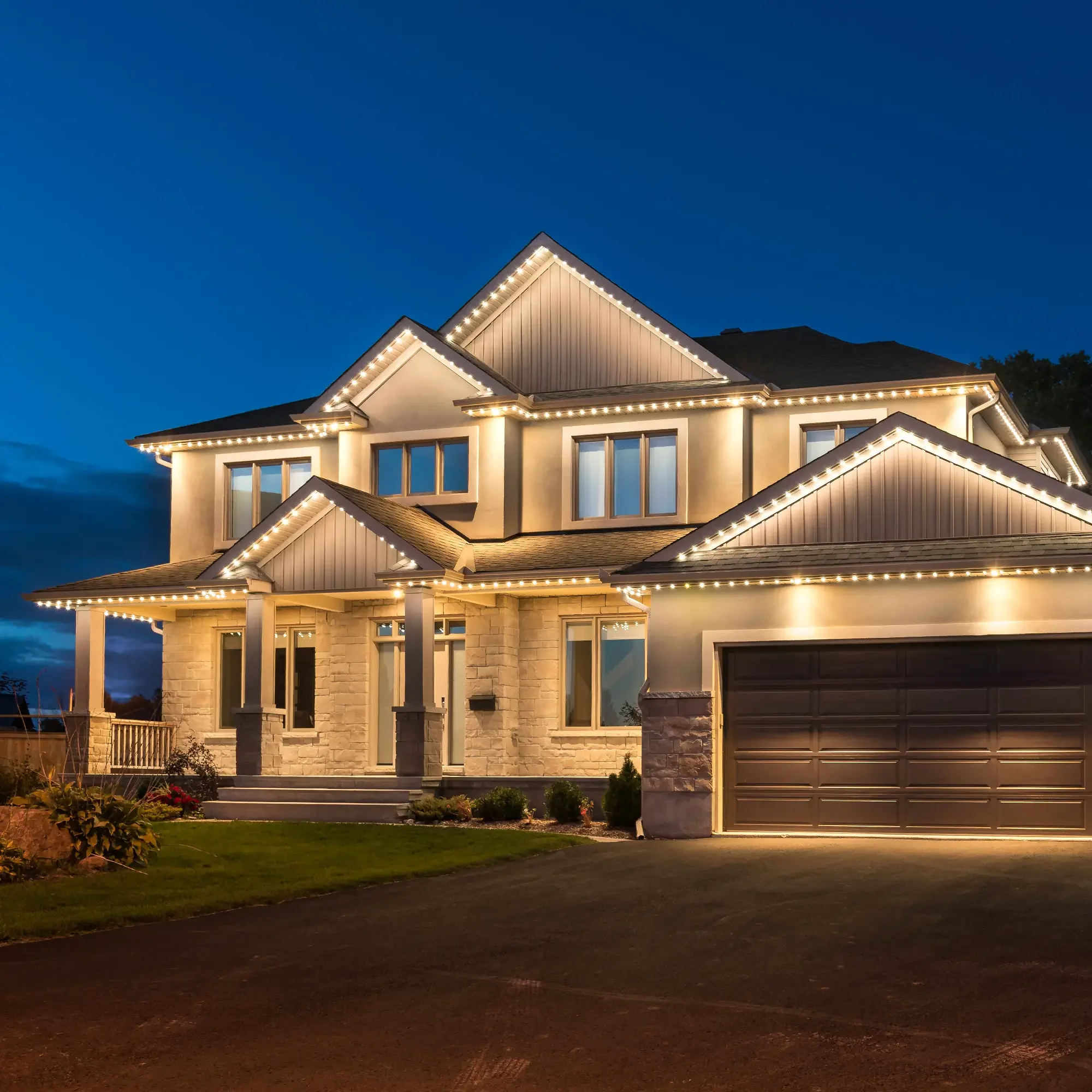 A well-lit, modern suburban house at dusk with exterior string lights, stone and siding facade, multiple windows, a porch, and a garage.
