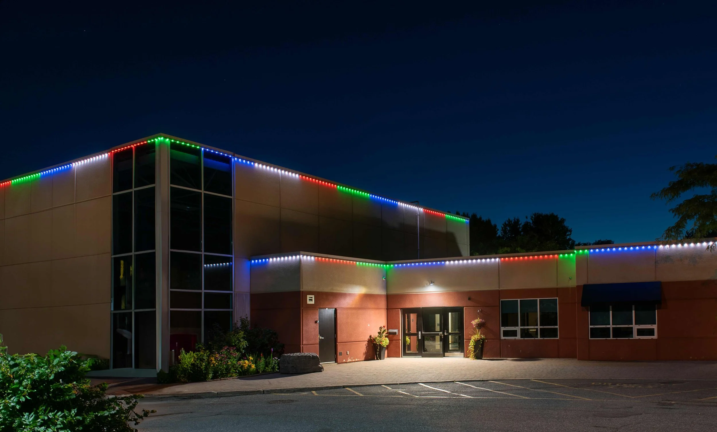 Nighttime view of a commercial building decorated with colorful string lights along the edges of its roof and upper walls.