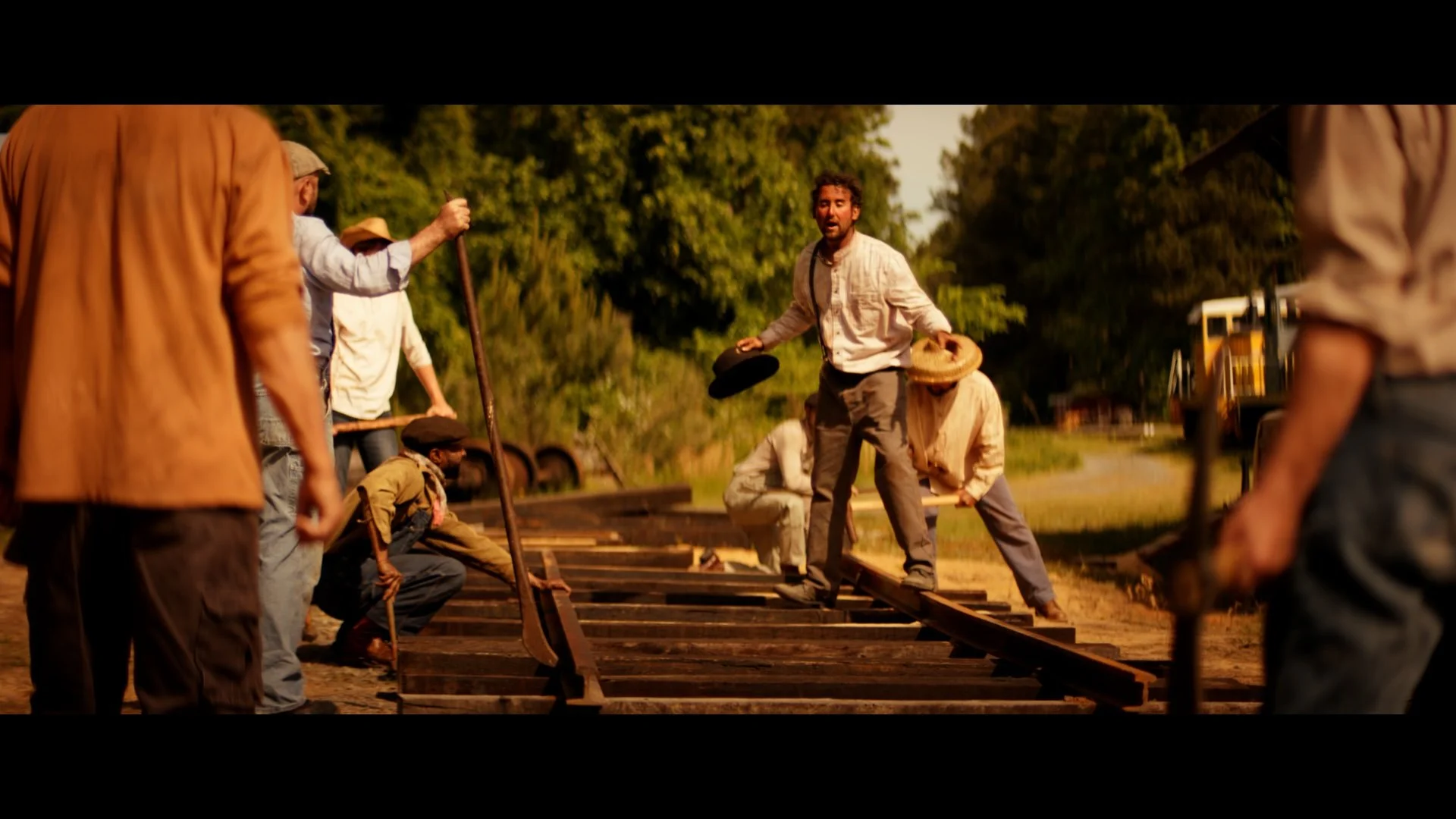 People working together to build a wooden train track outdoors during sunset.