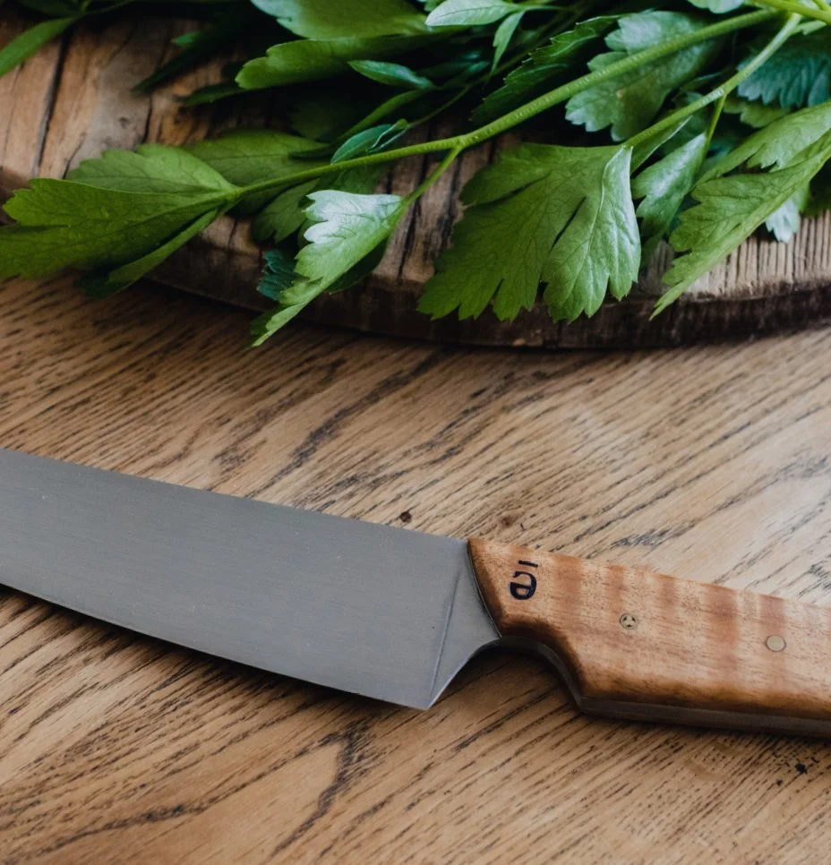 Wooden cutting board with fresh parsley and a chef's knife on a wooden table.