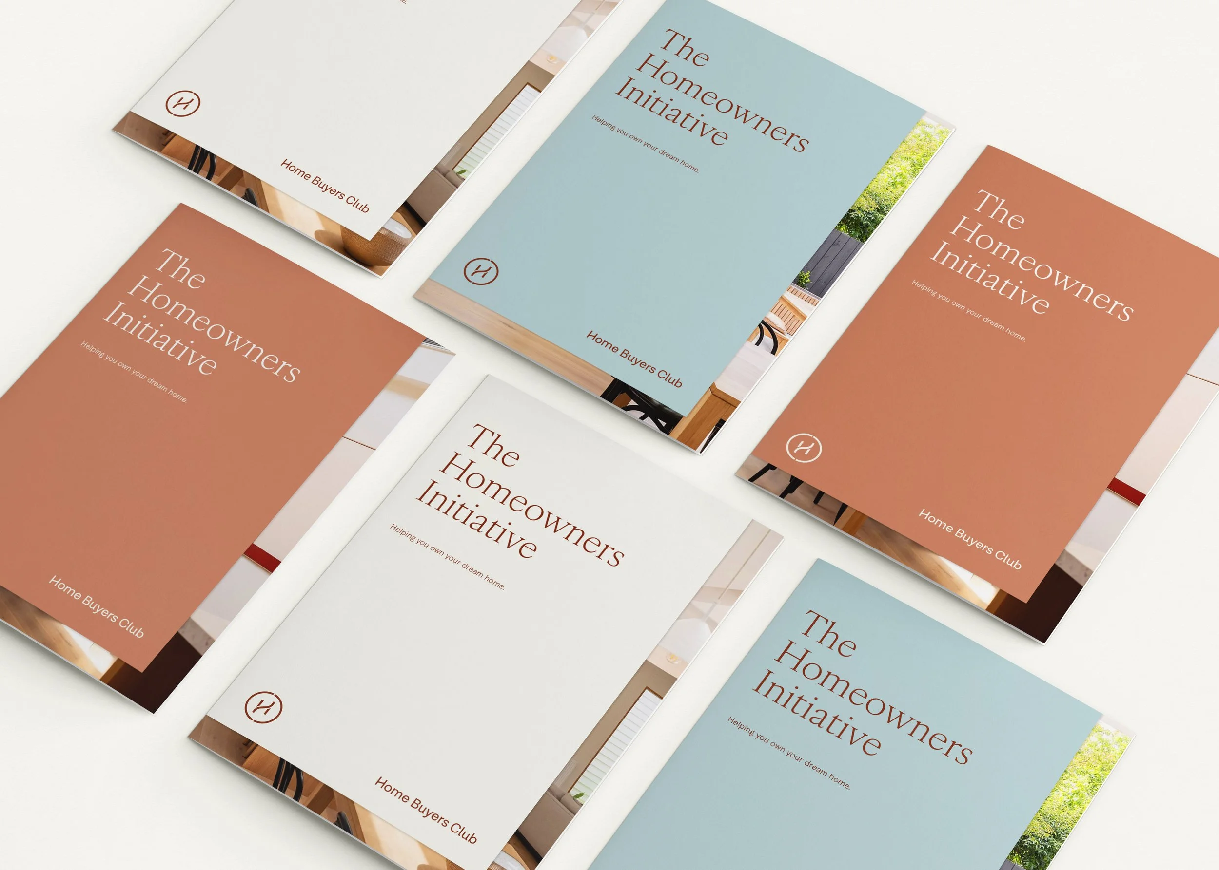 Brochures for 'The Homeowners Initiative' by Home Buyers Club with pastel blue, white, and terracotta-colored covers arranged on a white table.