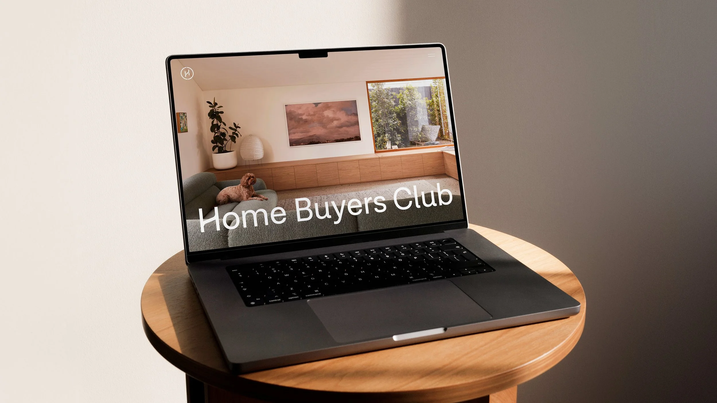 Laptop displaying a room with a sofa, a dog, a plant, a lamp, and a painting, with the text "Home Buyers Club" on the screen.