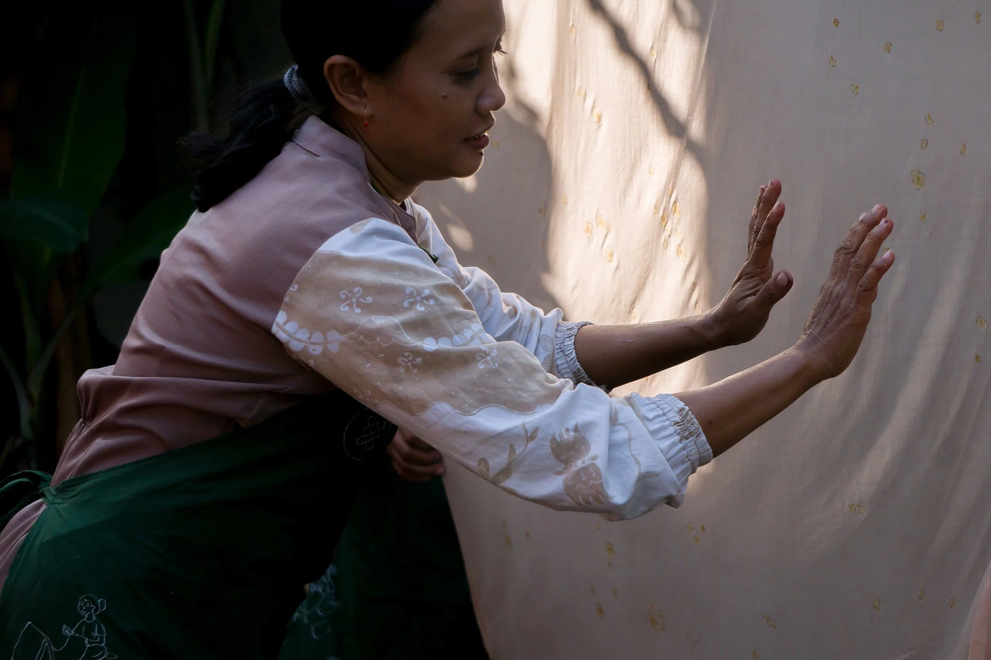 Woman pressing fabric against wall, wearing embroidered clothing, in outdoor setting.