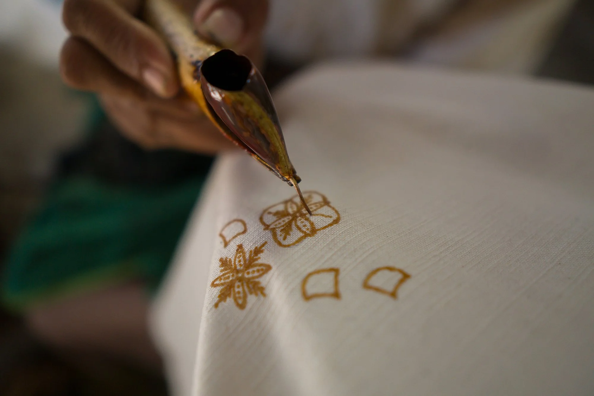 Close-up of a person using a canting tool to apply wax on fabric in a batik design process.