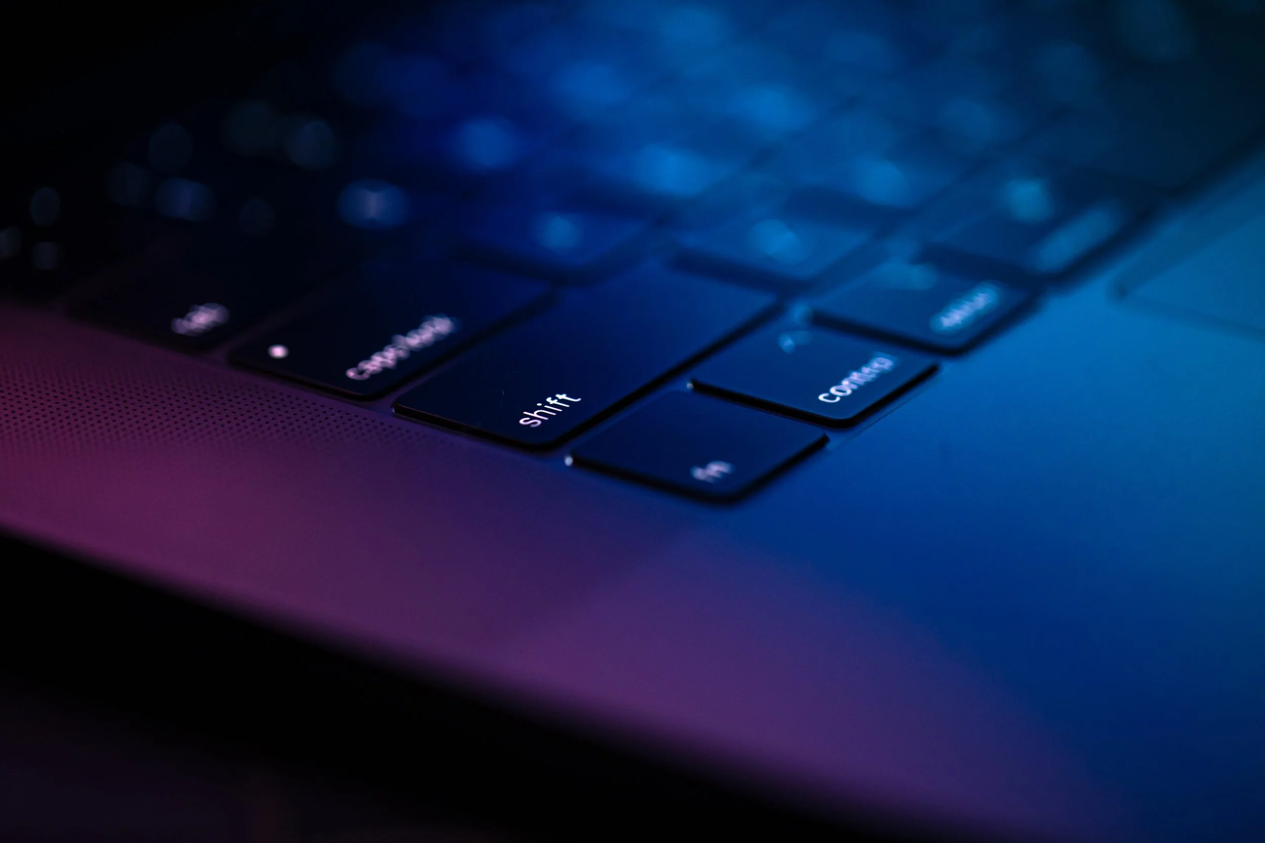 Close-up of a laptop keyboard illuminated with blue and purple lighting.