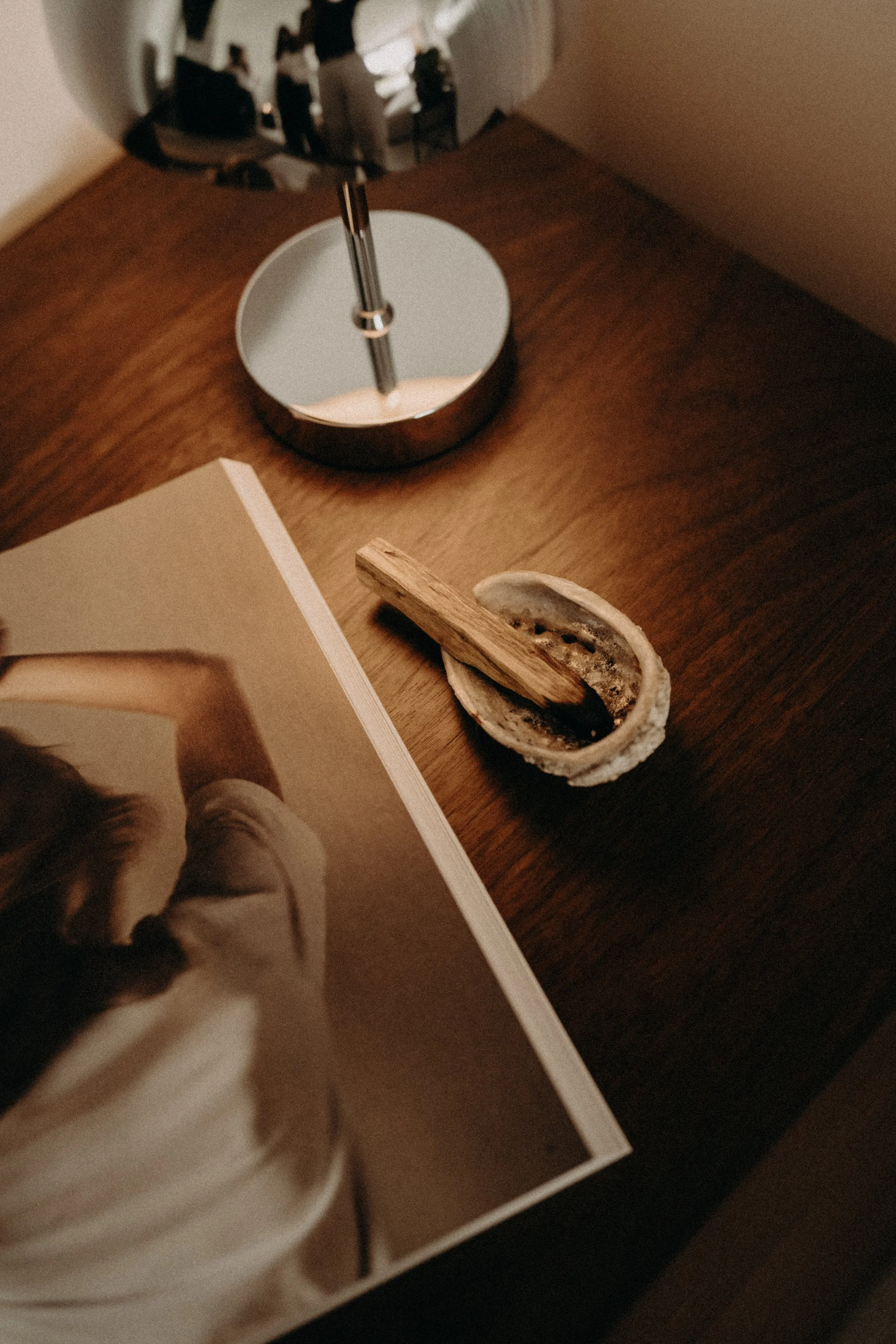 Une lampe de bureau en acier inoxydable sur une table en bois, un coquillage blanc et une photo ou une affiche en partie visible.